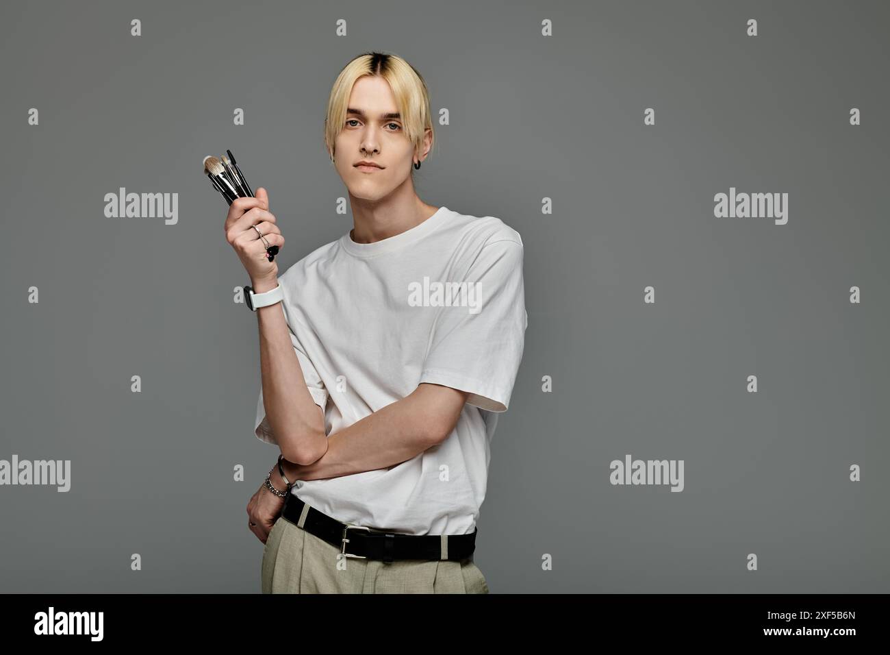 Uomo elegante in un outfit alla moda con una custodia compatta piena di spazzole per il trucco. Foto Stock