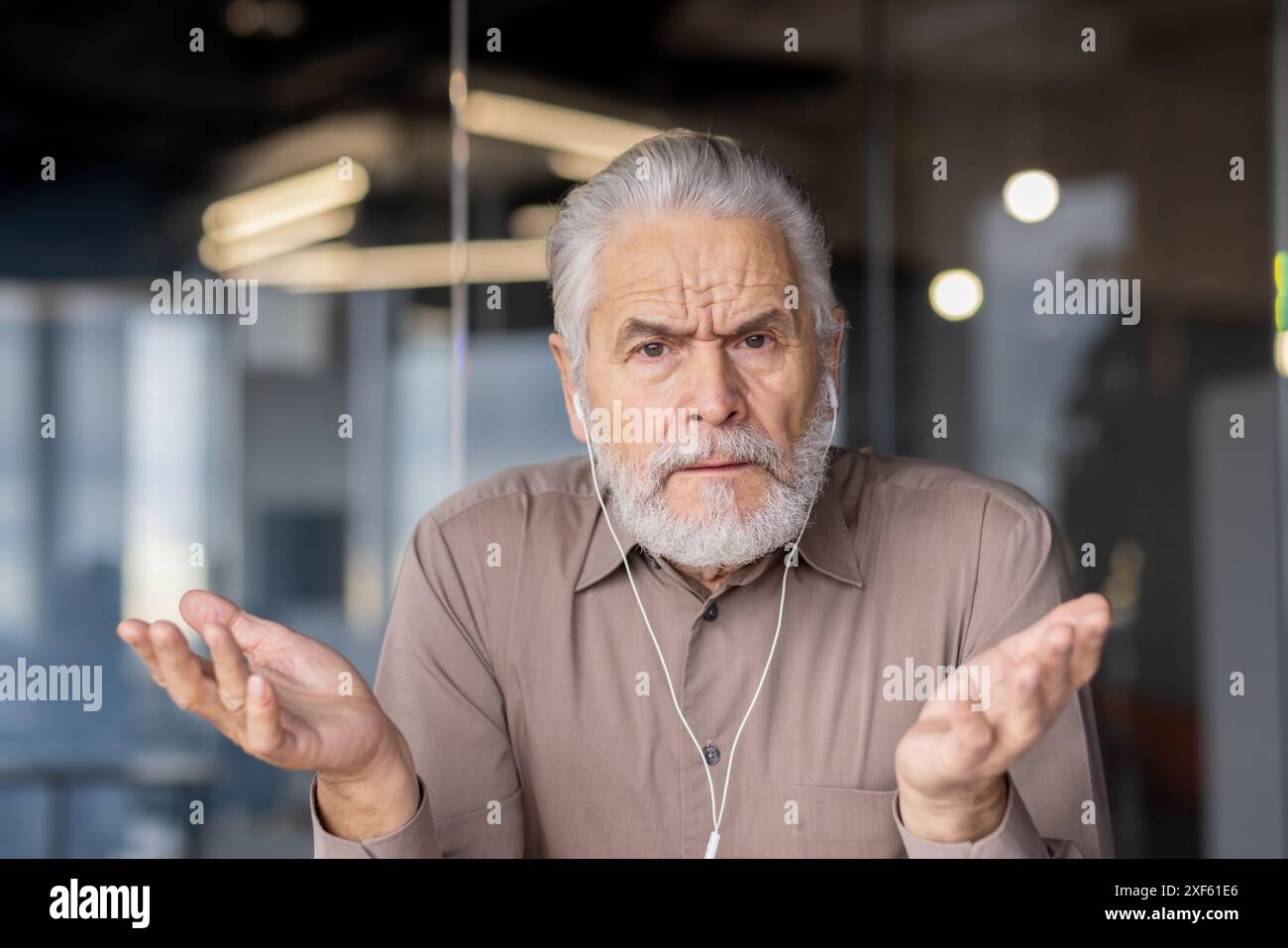 Un uomo d'affari anziano con un'espressione confusa si toglie le spalle durante un incontro virtuale in un ufficio moderno. L'immagine cattura i sentimenti di incertezza e comunicazione sul luogo di lavoro Foto Stock