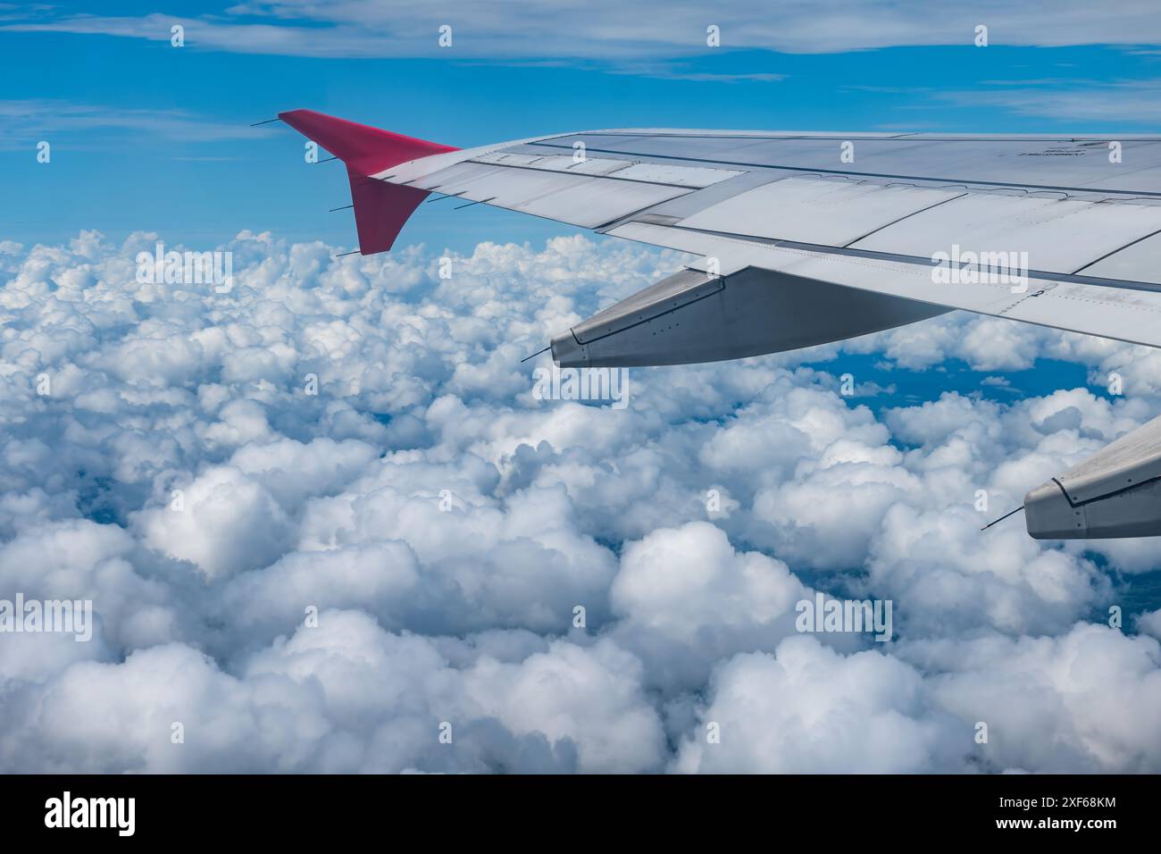 Vista dalla finestra dell'aeroplano delle nuvole soffici e del cielo blu luminoso con ala dell'aeroplano Foto Stock