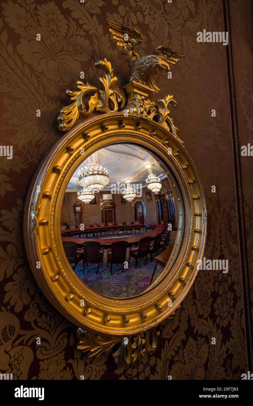 Uno specchio dorato sormontato da un aquila è appeso alla parete della Sala del Senato nel Municipio di Brema. Riflette il tavolo rotondo con sedie in pelle e i due lampadari di cristallo della stanza. La parete dietro di esso è ricoperta di seta damascata a motivi rosso-marrone. Brema, Germania. Foto Stock