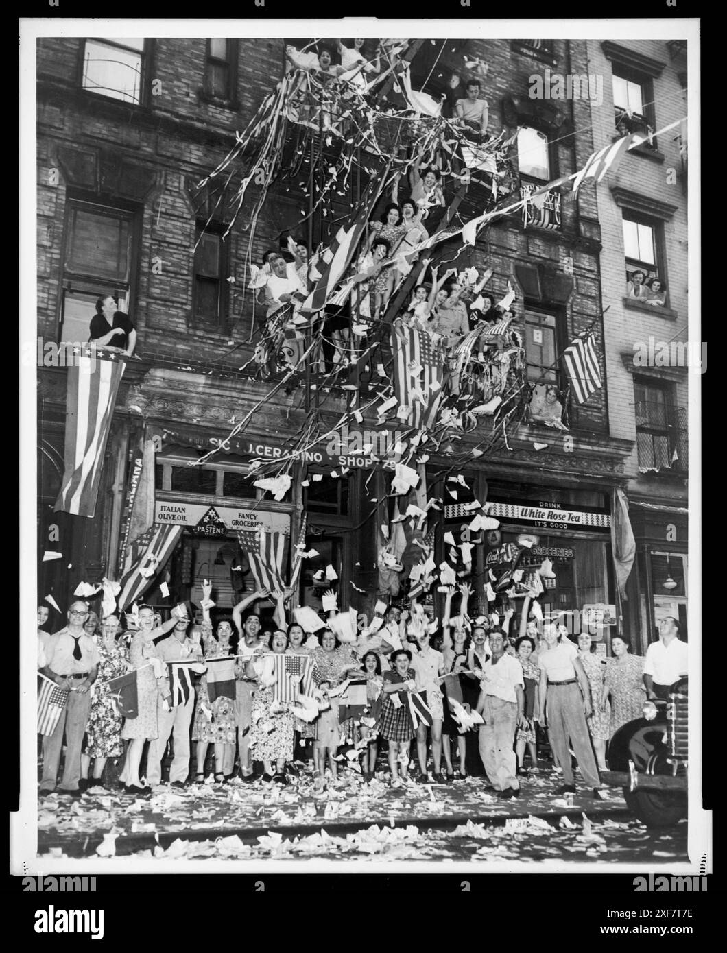 Esuberanti residenti della Little Italy di New York di fronte al 76 di Mulberry St, salutano la notizia dell'accettazione giapponese dei termini di resa alleati con bandiere ondulate e una pioggia di carta, New York, New York, 14 agosto 1945. Foto di New York World-Telegram e The Sun Newspaper Photograph Collection Foto Stock