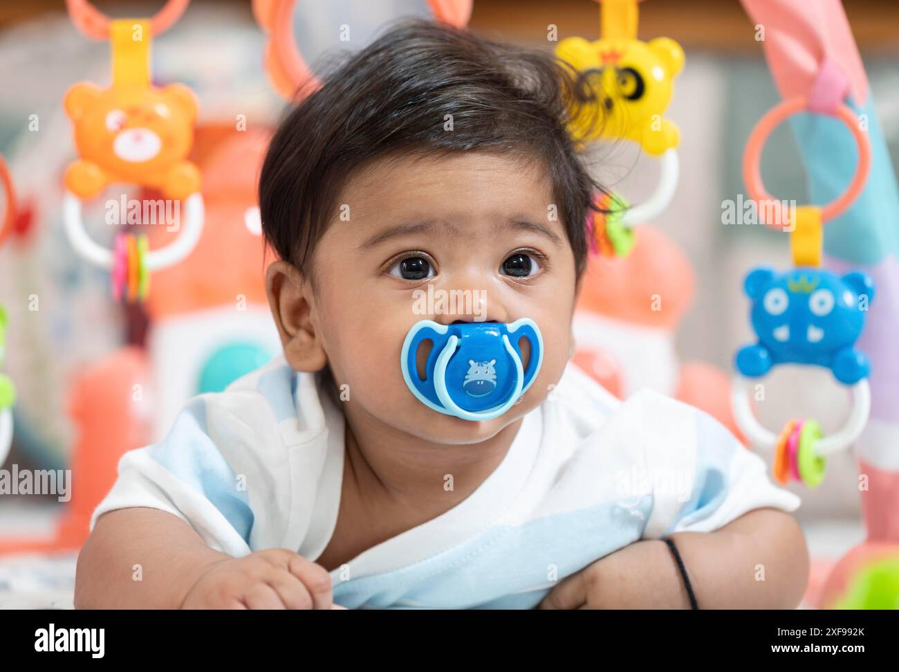 Bambino che gioca sdraiato sul letto con il succhietto sulla bocca Foto Stock