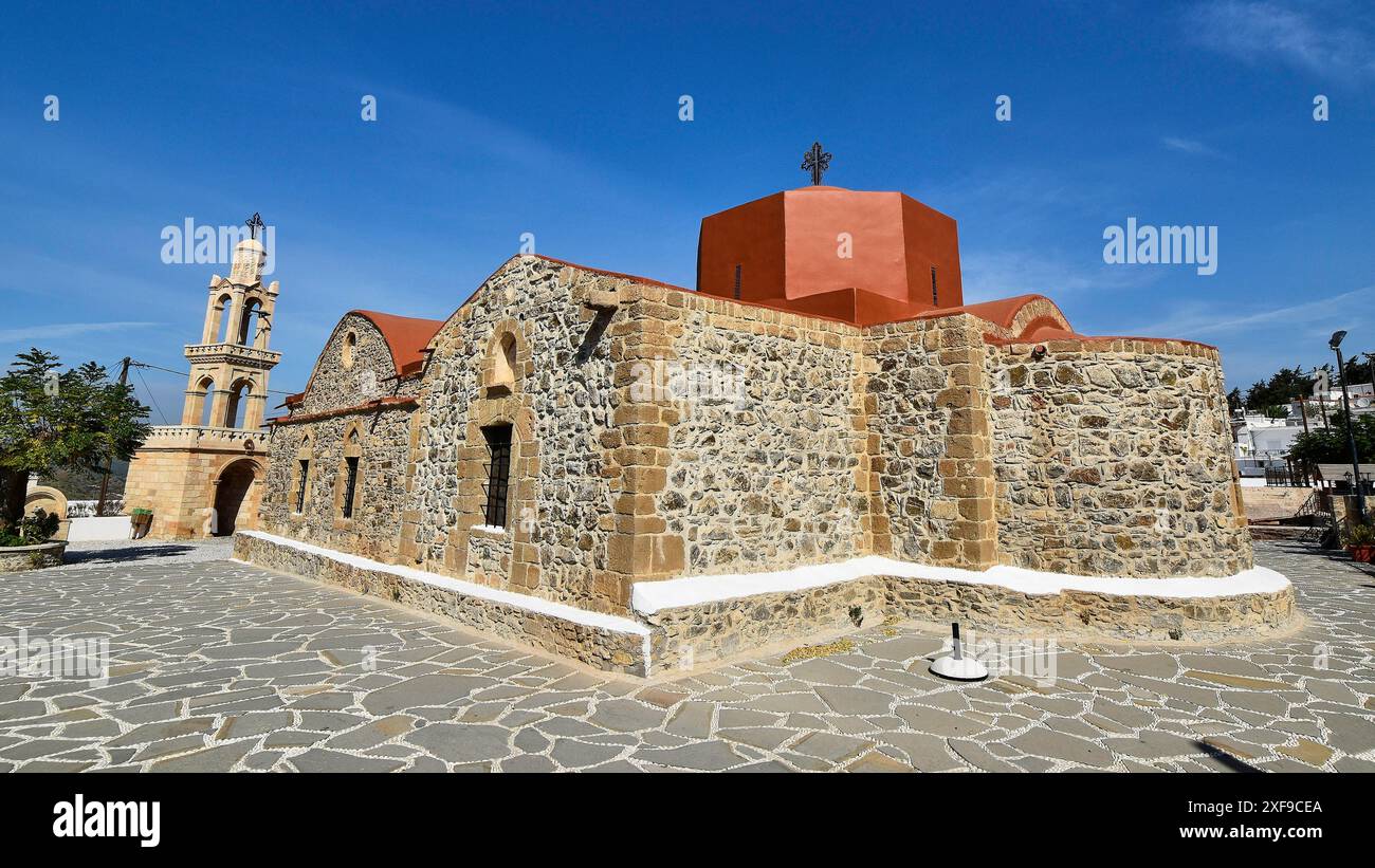 Vista laterale di un'antica chiesa in pietra con una torre e un campanile sotto un cielo blu in una giornata di sole, del villaggio di Asklipio, di Asklipion, Kimisis tis Theotokou Foto Stock