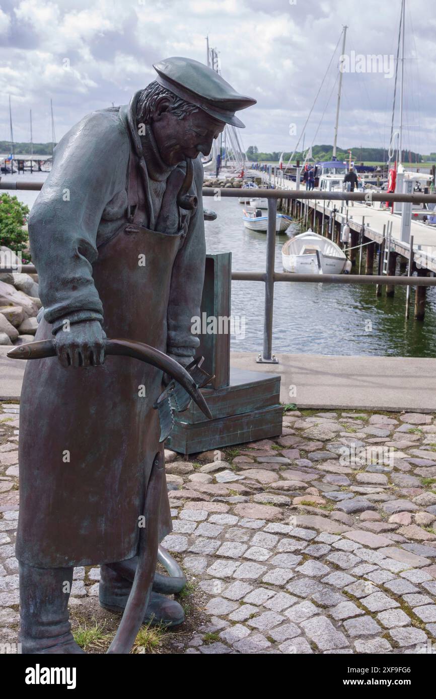 Statua in bronzo di un pescatore al porto, passerella pavimentata e barche sullo sfondo, maasholm, germania Foto Stock