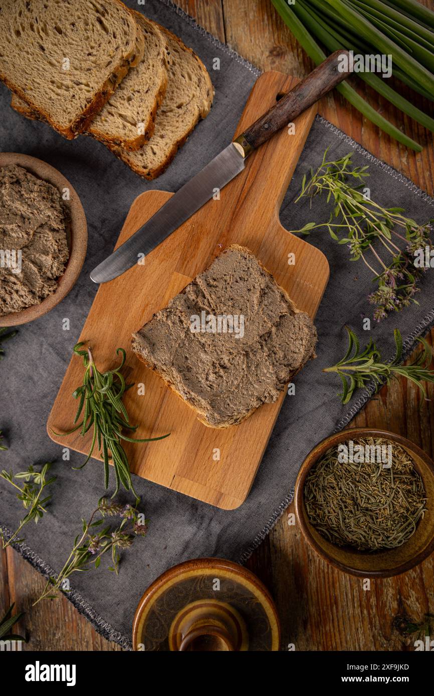 Pate di fegato servito su un tavolo rustico con pane ed erbe fresche, vista dall'alto Foto Stock