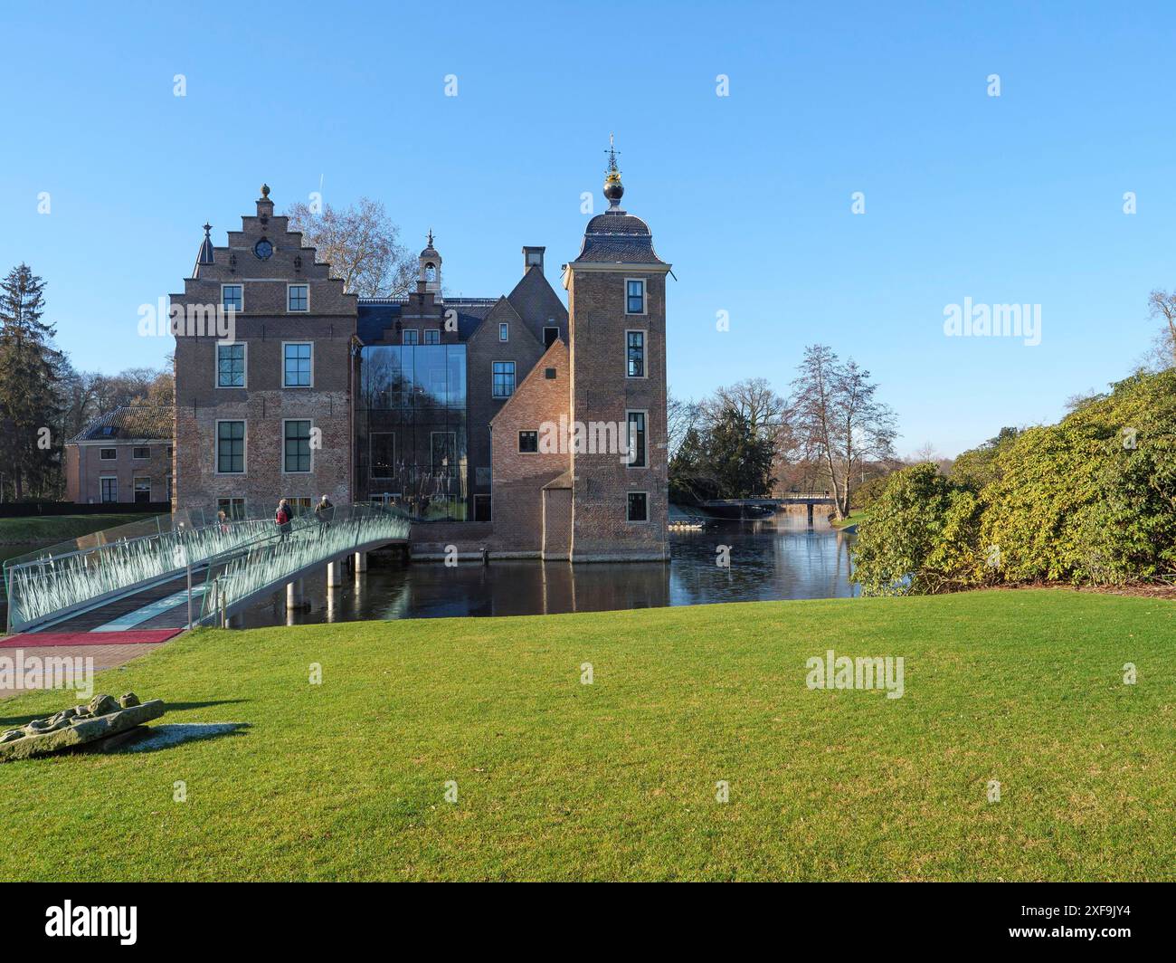 Un castello storico con un moderno ponte di vetro su un corpo d'acqua in un paesaggio verde ben curato in una giornata di sole, Ruurlo, gheldria, paesi bassi Foto Stock