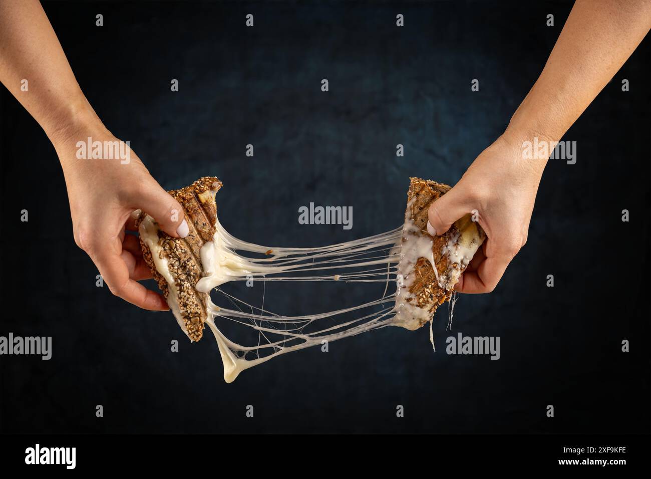 Due mani separano un sandwich al formaggio alla griglia con il formaggio fuso che si estende tra le due metà Foto Stock
