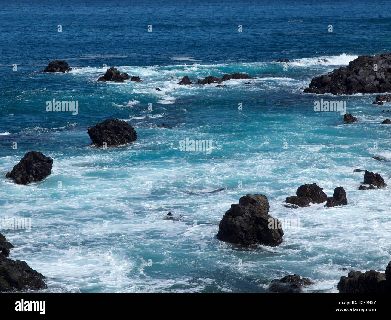 Scenario marino con rocce nell'acqua e schiuma ondulata sotto un cielo blu, puerto de la cruz, tenerife, spagna Foto Stock