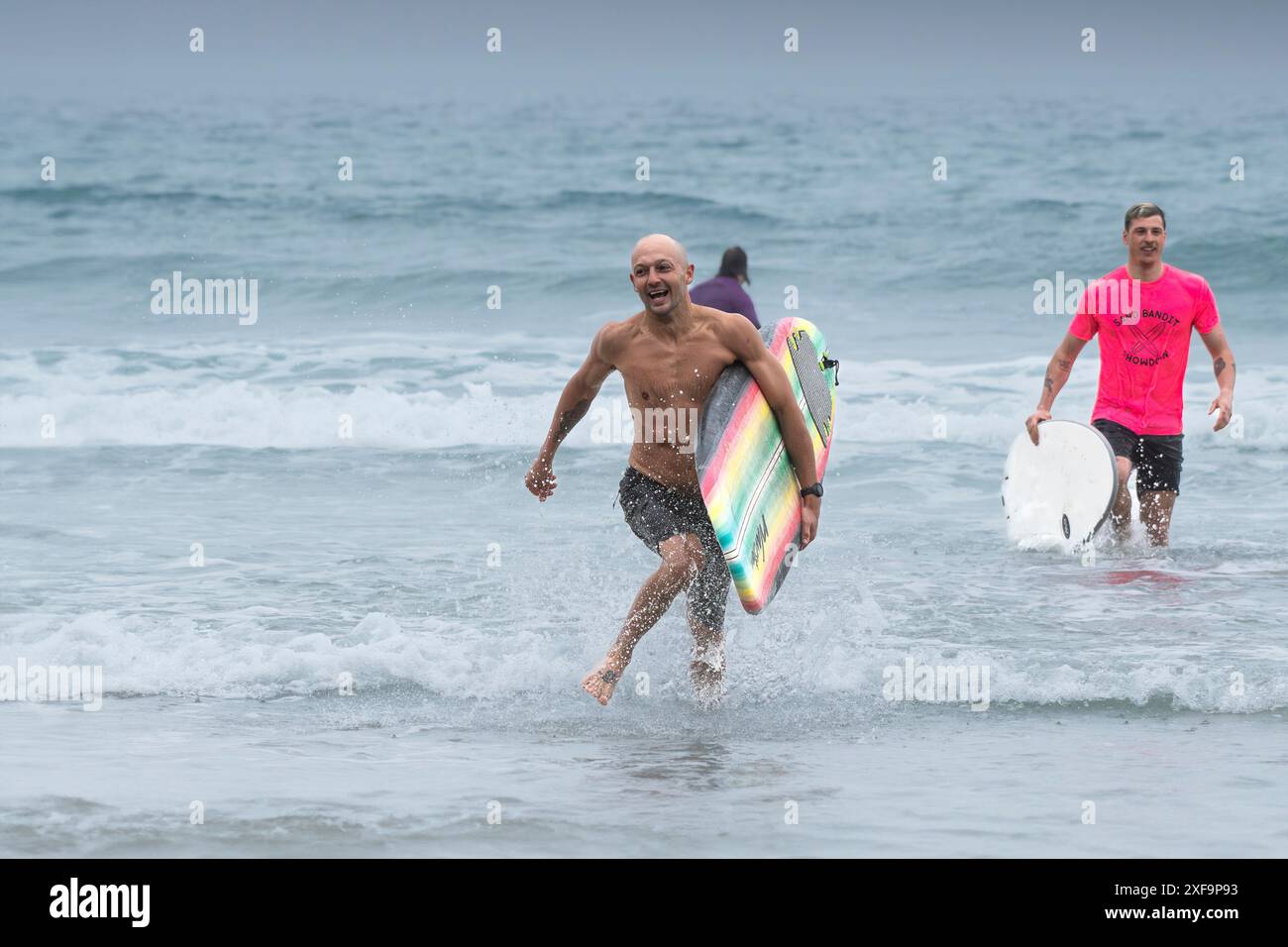 Surfers che corrono fuori dal mare durante la gara di surf Sand Bandit Showdown al GT Western Great Western Beach di Newquay in Cornovaglia nel Regno Unito. Foto Stock