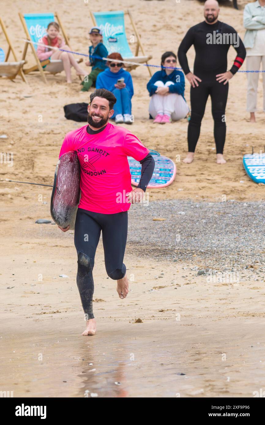 Un surfista sorridente che corre in mare durante la gara di surf Sand Bandit Showdown al GT Western Great Western Beach di Newquay in Foto Stock