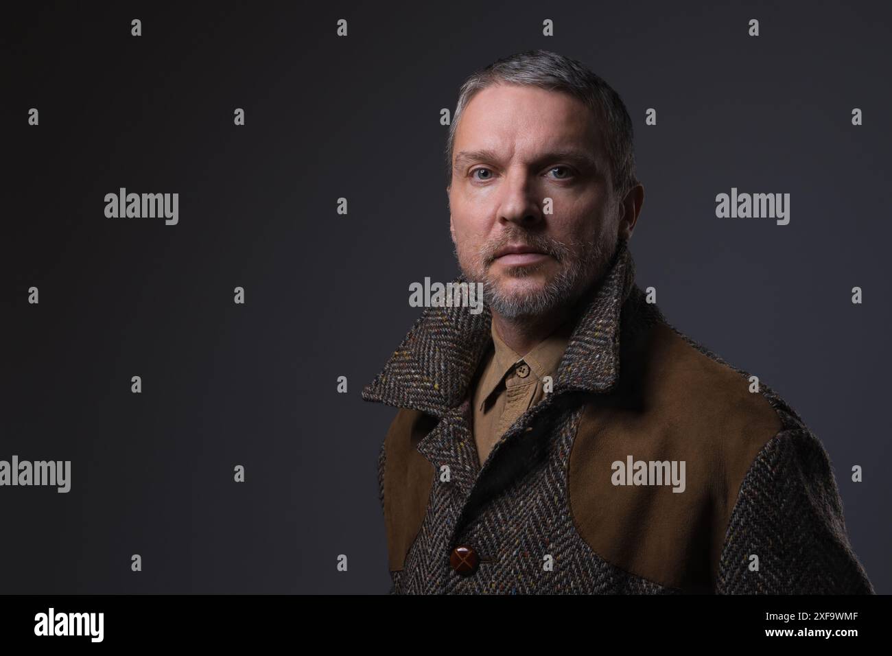 Faccia seria di un uomo di mezza età con la barba che guarda la fotocamera. Ritratto ravvicinato di un triste cinquant'anni su uno sfondo scuro. Problema Foto Stock