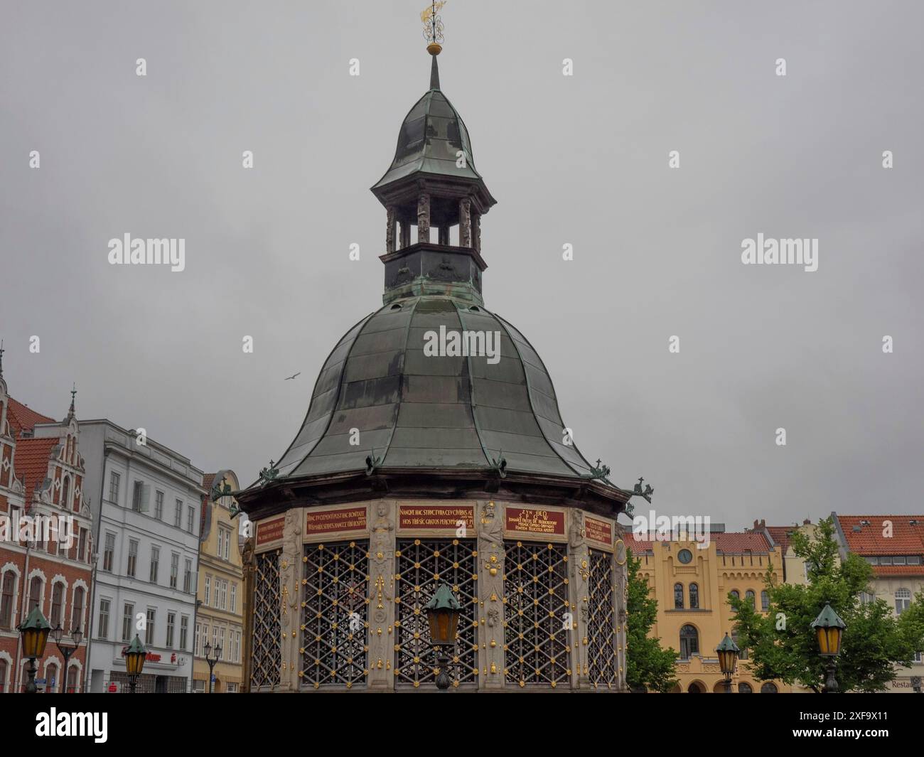 Storica fontana nel centro della città con un reticolo ornato e un tetto di rame sotto un cielo grigio, Wismar, Mar Baltico, Germania Foto Stock