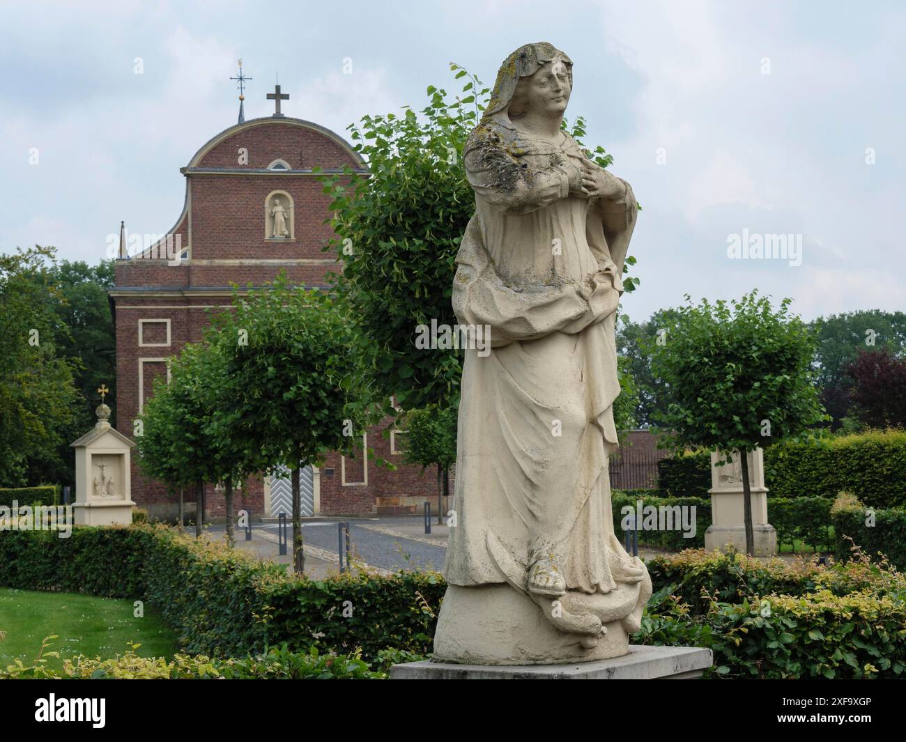 Statua in pietra di una donna di fronte a una chiesa con un giardino ben tenuto sullo sfondo, atmosfera limpida e tranquilla, Vreden, Renania settentrionale-Vestfalia Foto Stock