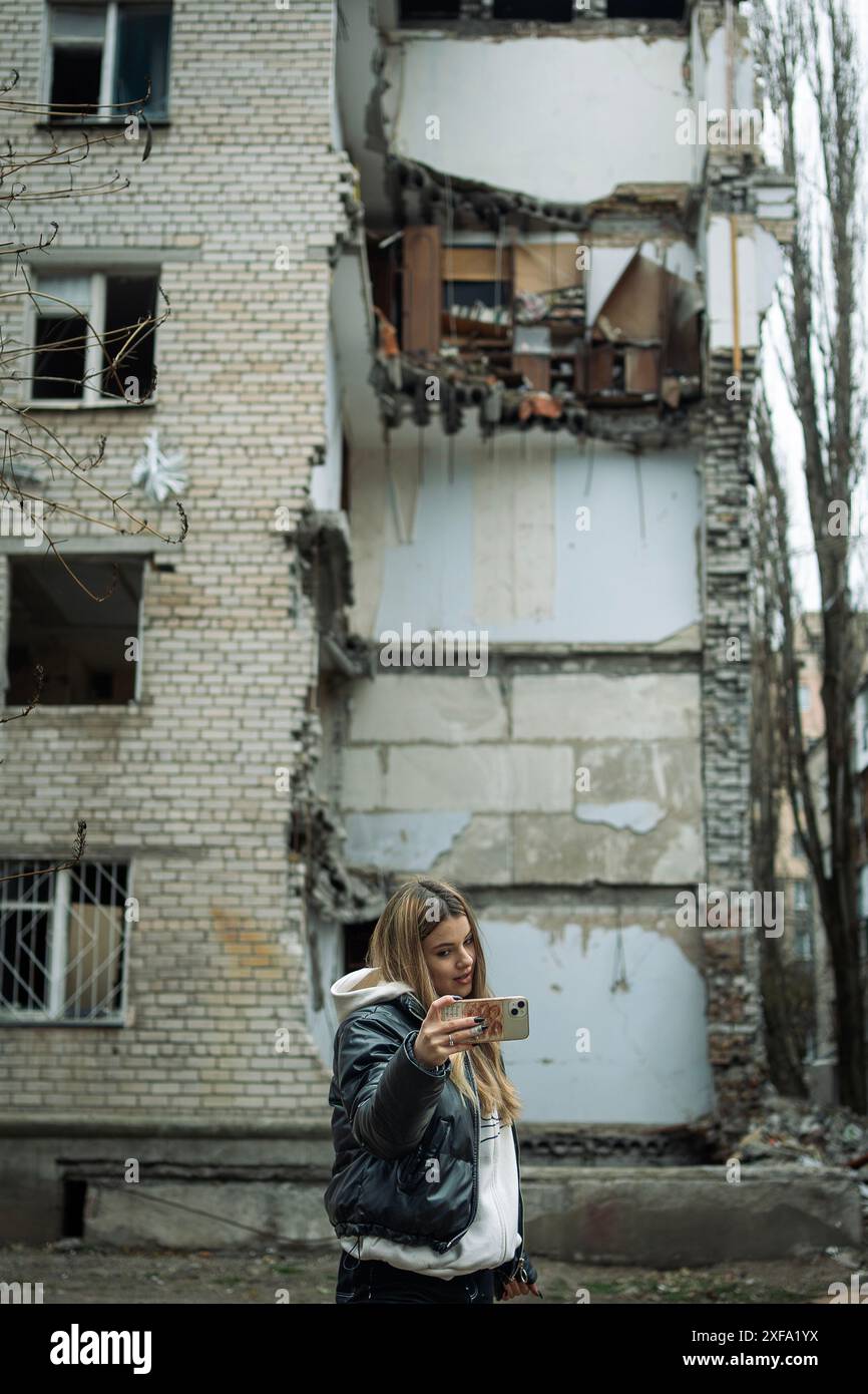 Una giovane ragazza si fa un selfie di fronte a un edificio distrutto dai bombardamenti a Mykolaiv, Ucraina. Foto Stock