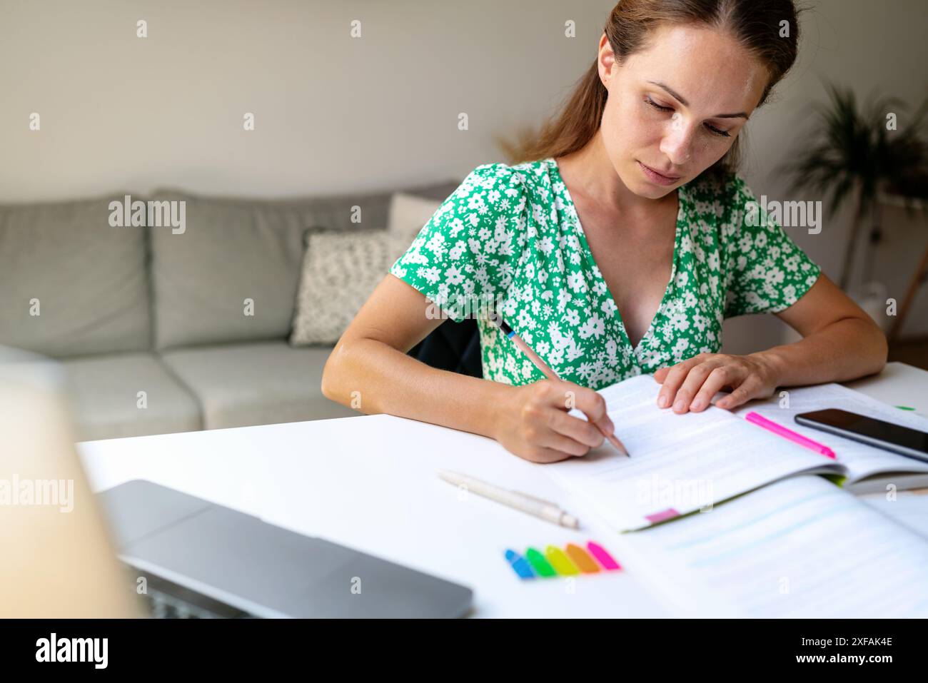 Una bruna in un abito estivo verde si siede a un tavolo e scrive su un taccuino. Studente adulto, formazione continua. Foto Stock