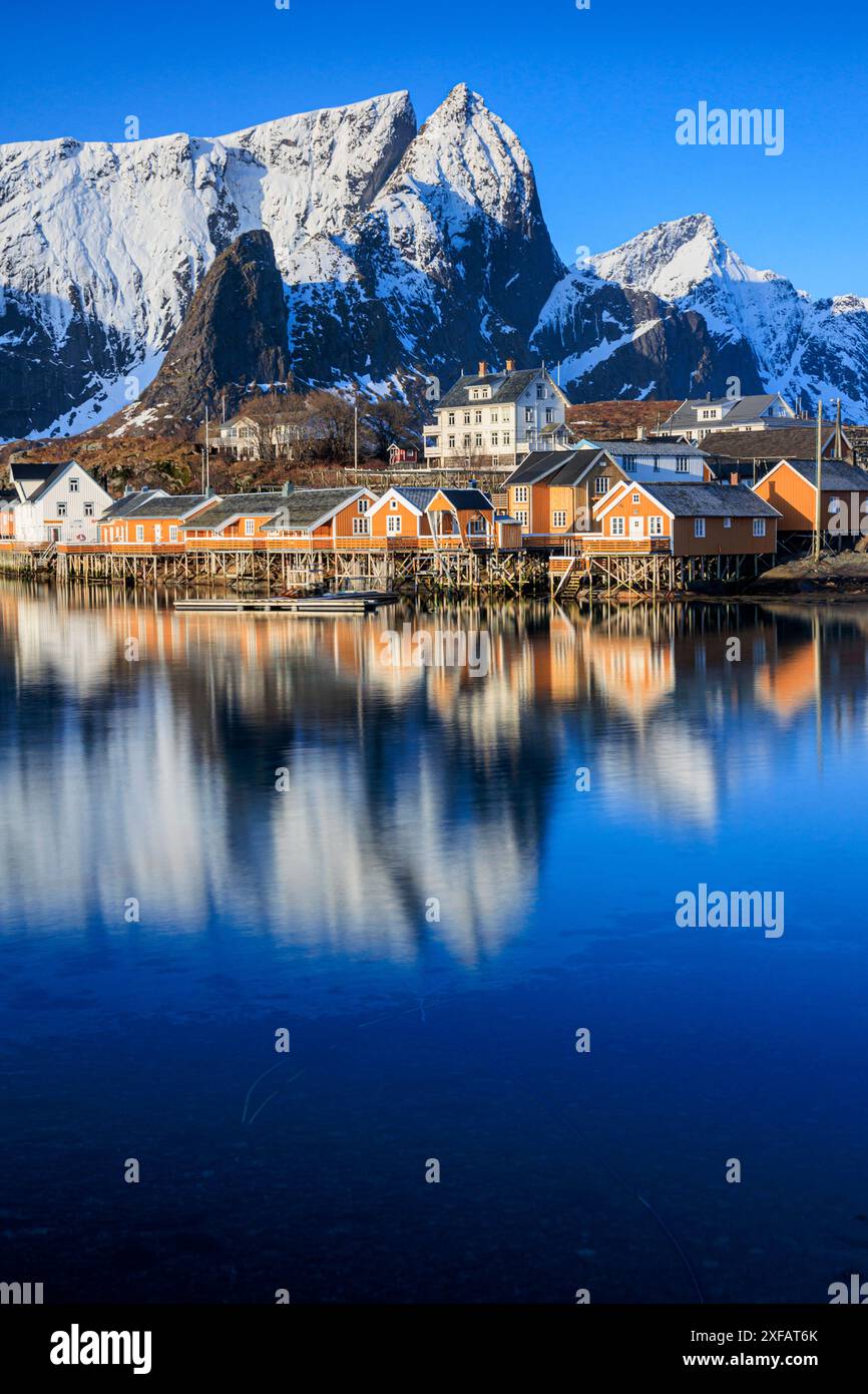 Case rosse e villaggio di fronte a montagne innevate, fiordo, alba, Reine, Moskenesoya, Lofoten, Norvegia, Europa Foto Stock