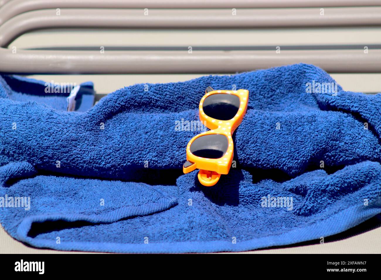 Colori gratuiti di un telo da spiaggia blu e occhiali da sole con cornice arancione, posti per prenotare un lettino solare sul ponte di una nave da crociera. Foto Stock