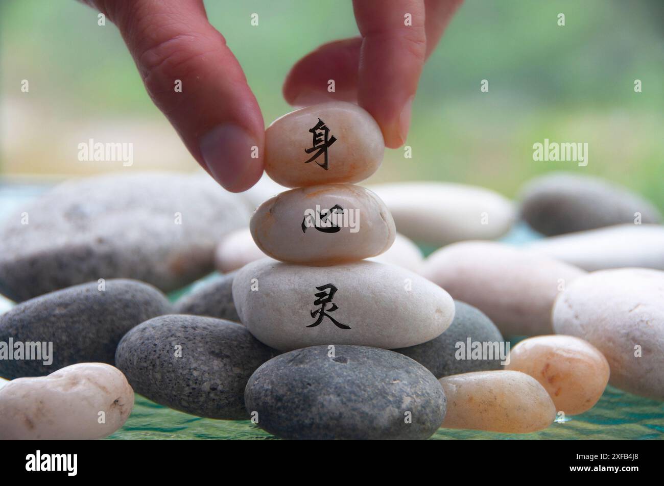 Mano che posiziona la pietra Zen con corpo, mente e spirito in carattere cinese. Concetto Zen. Foto Stock