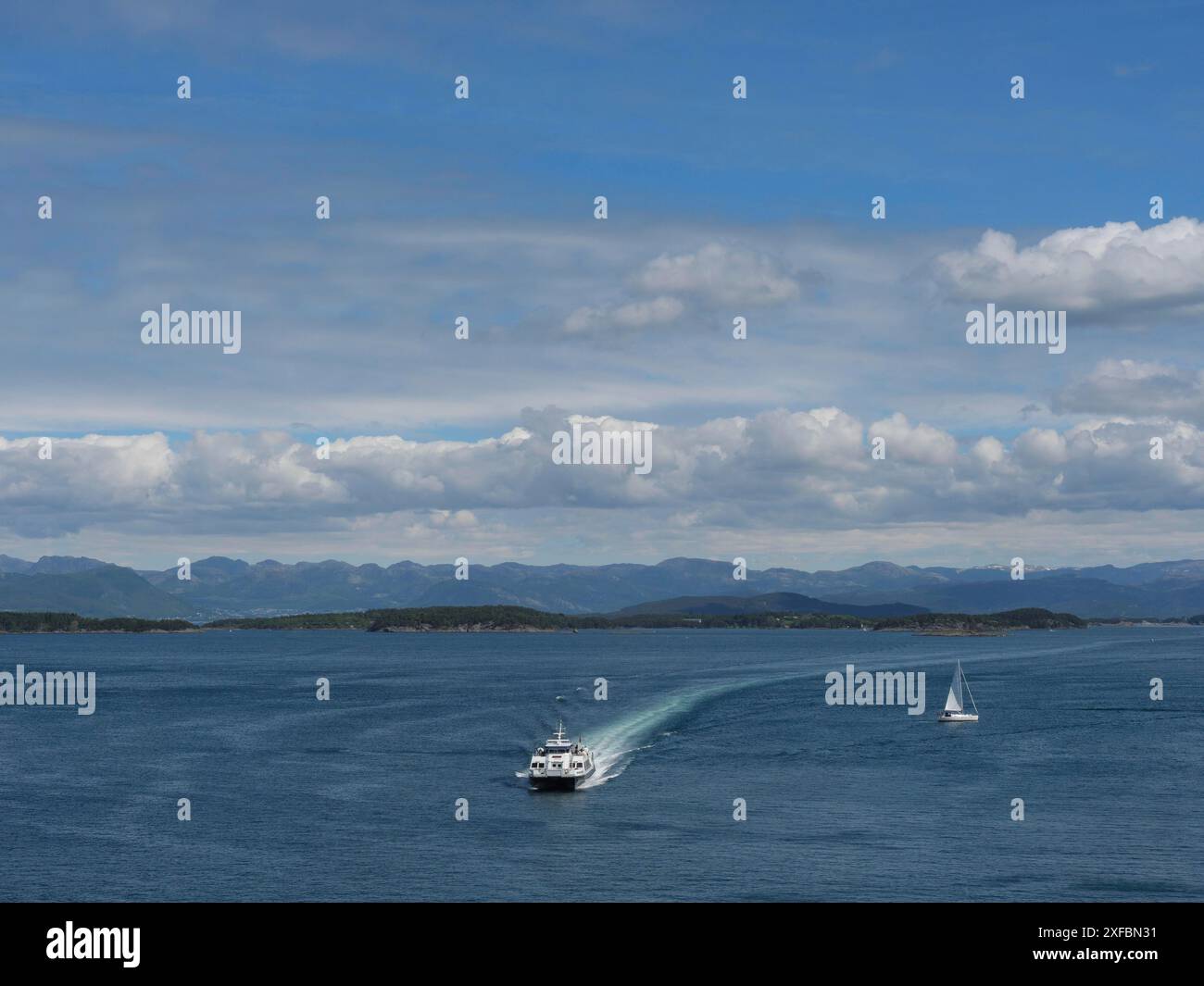 Un traghetto e una barca a vela che navigano sul mare, circondati da isole e montagne sotto un cielo blu con alcune nuvole, stavanger, norvegia Foto Stock