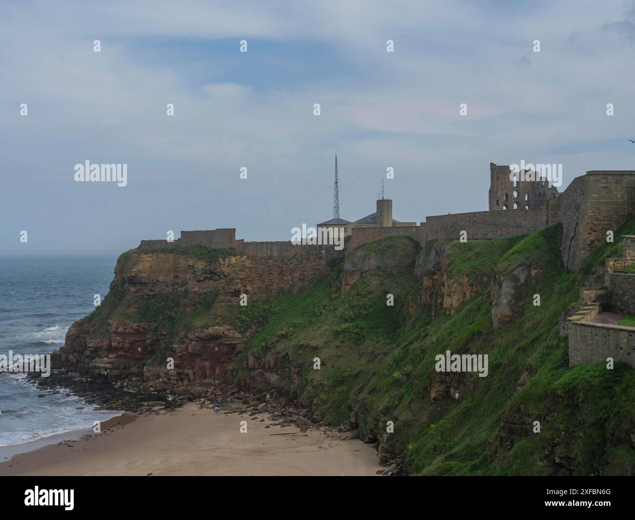 Vista di un edificio e rovine su una scogliera verde con mare sullo sfondo sotto un cielo nuvoloso, tynemouth, inghilterra, Regno Unito Foto Stock