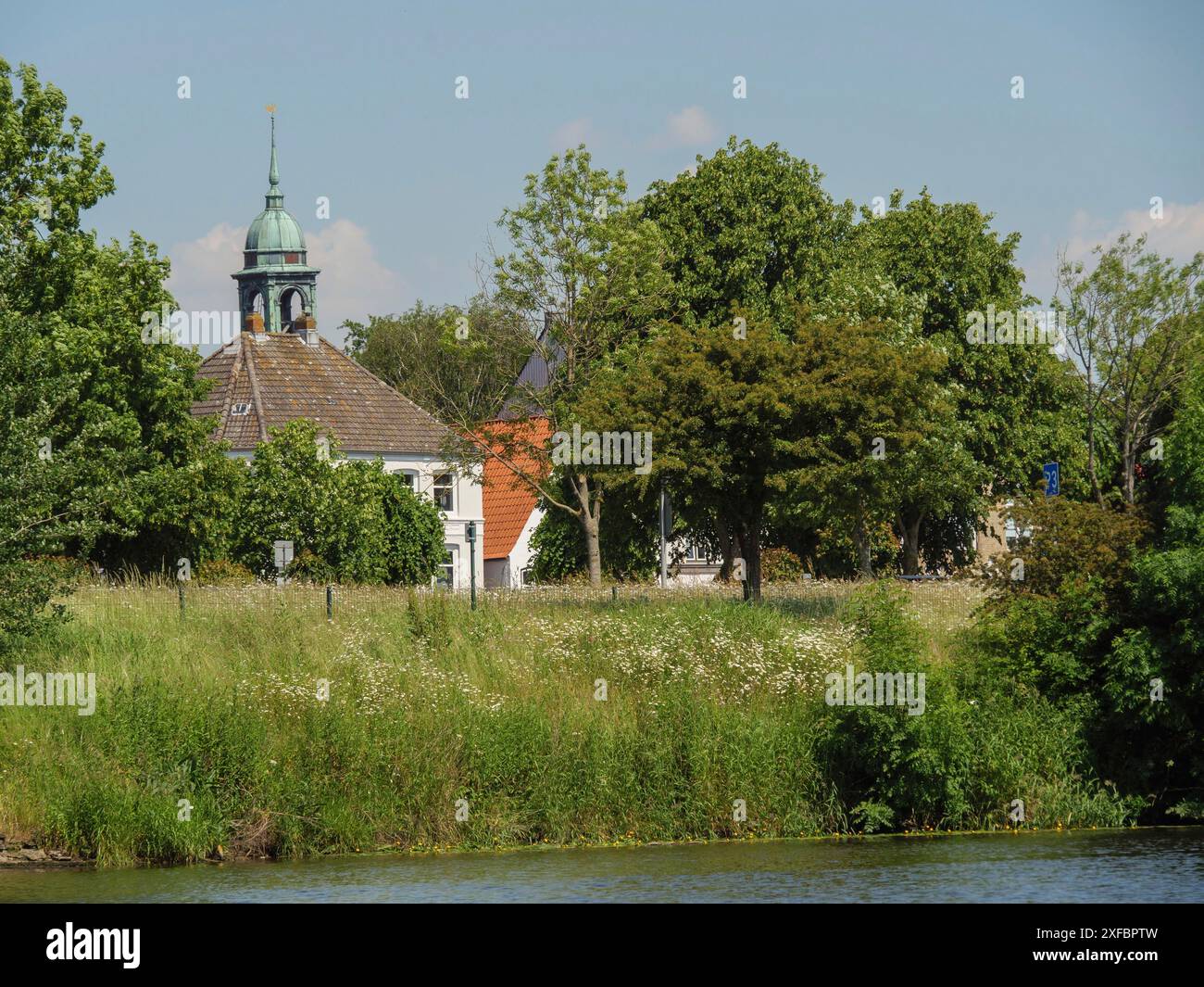 Paesaggio verde idilliaco con una chiesa e altri edifici all'orizzonte, circondato da alberi lussureggianti, friedrichstadt, schleswig-holstein, germania Foto Stock