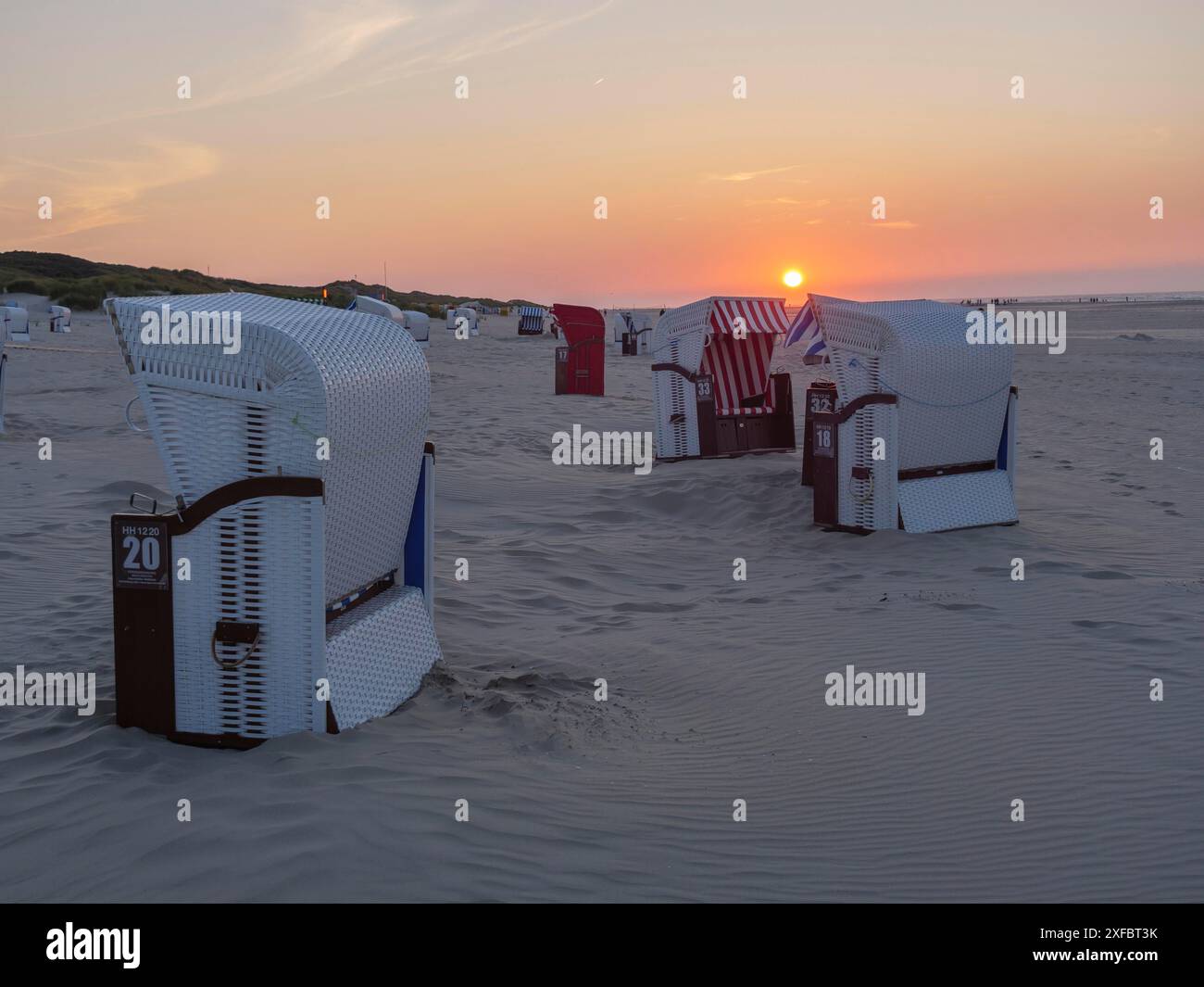 Tramonto sulla spiaggia con diverse sedie a sdraio. Il sole tramonta all'orizzonte sul mare, juist, frisia orientale, germania Foto Stock