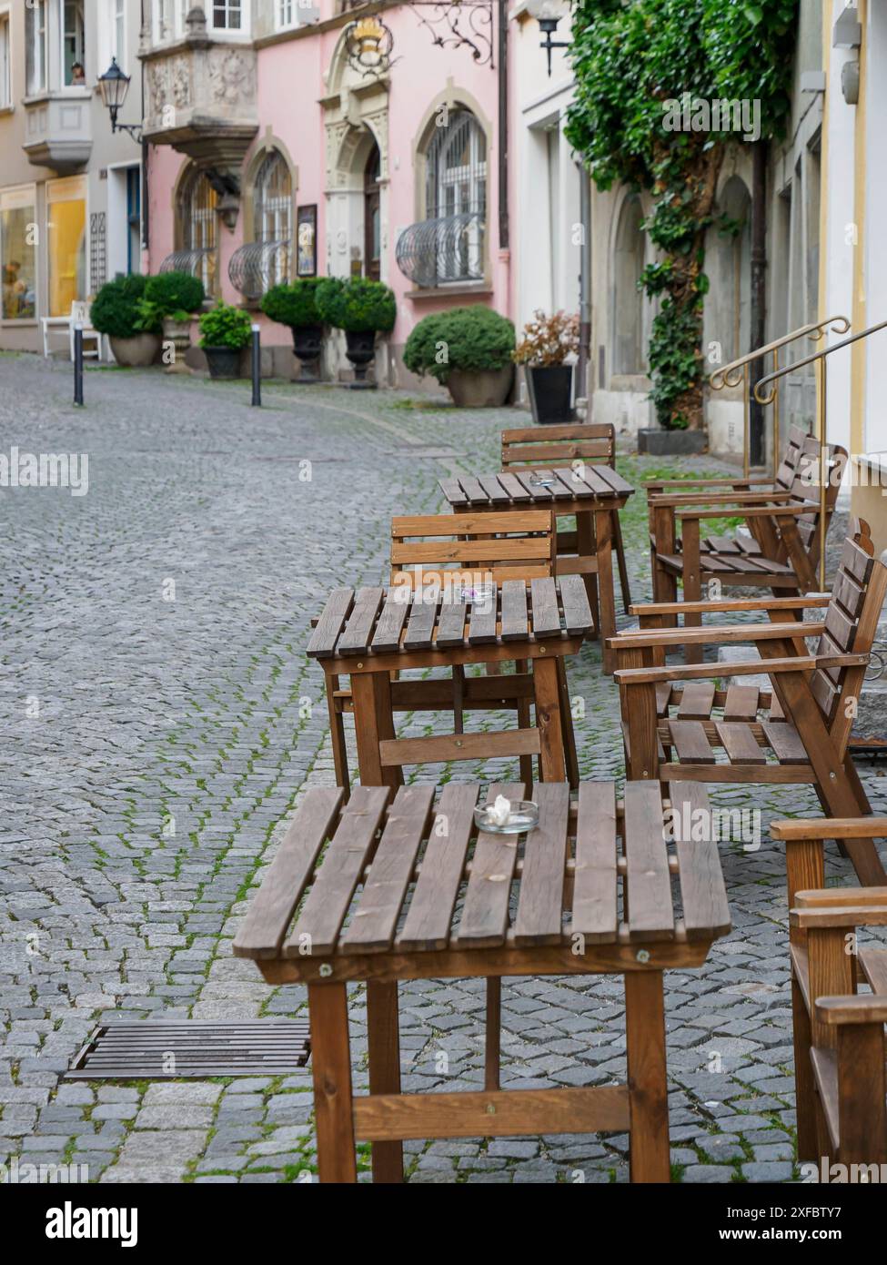 Tavoli e sedie vuoti in legno su una strada acciottolata in una zona tranquilla della città vecchia, lindau, baviera, germania Foto Stock