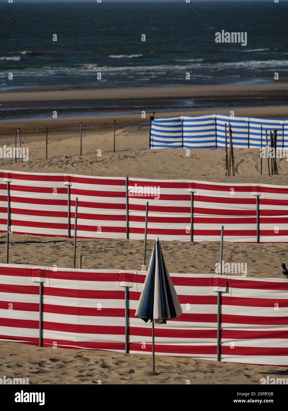 Numerose sedie a sdraio rosse e bianche e una blu e bianca sulla spiaggia sabbiosa di fronte al mare ventoso, De Haan, Fiandre, Belgio Foto Stock