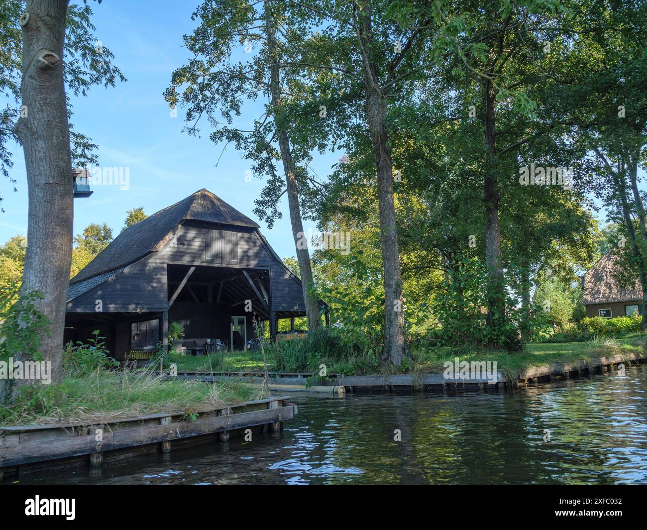 Una casa sull'acqua con un molo di legno, circondata da alberi verdi e una tranquilla atmosfera naturale, Giethoorn, Paesi Bassi Foto Stock