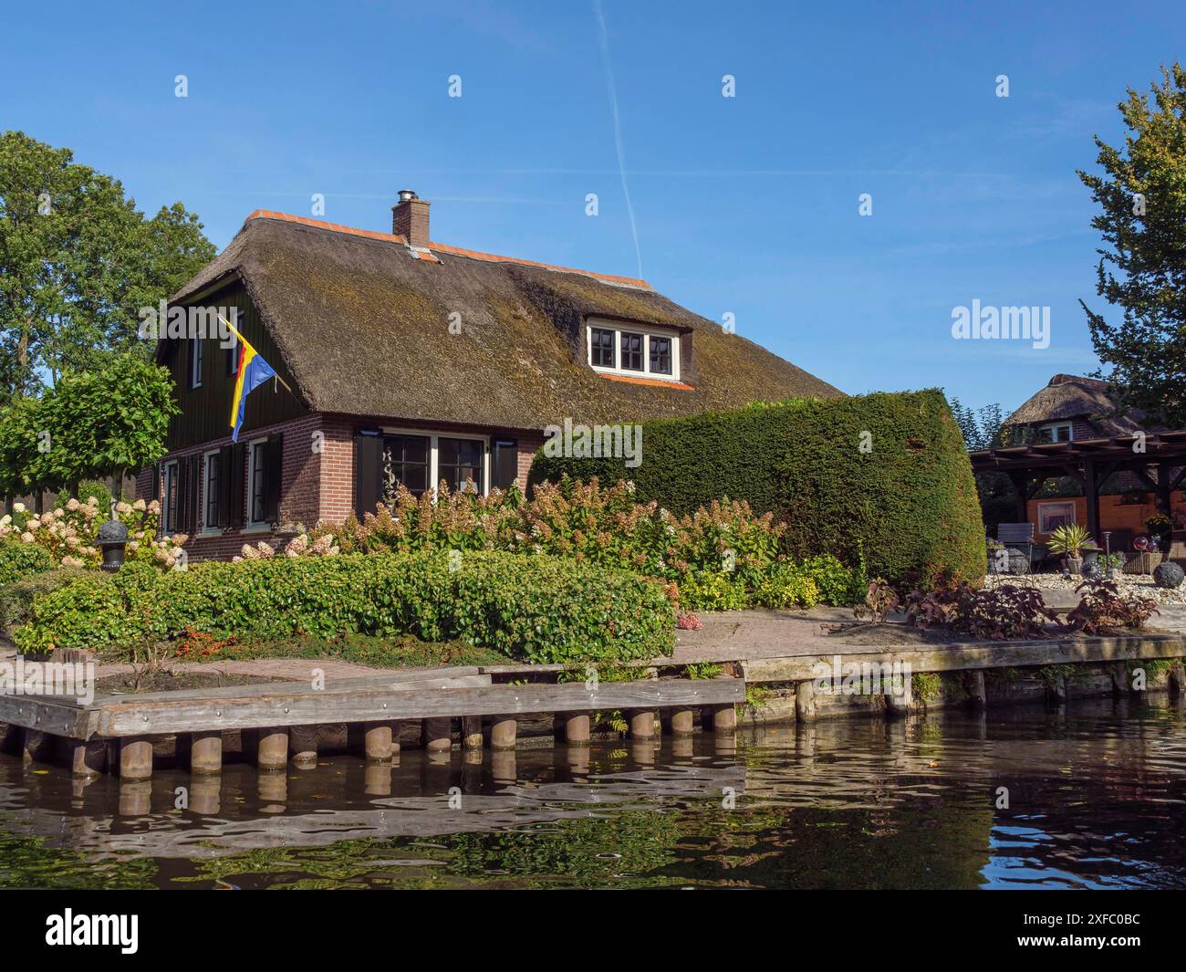 Casa con tetto in paglia e giardino ben tenuto sulla riva del canale, circondata da siepi e alberi, giethoorn, paesi bassi Foto Stock