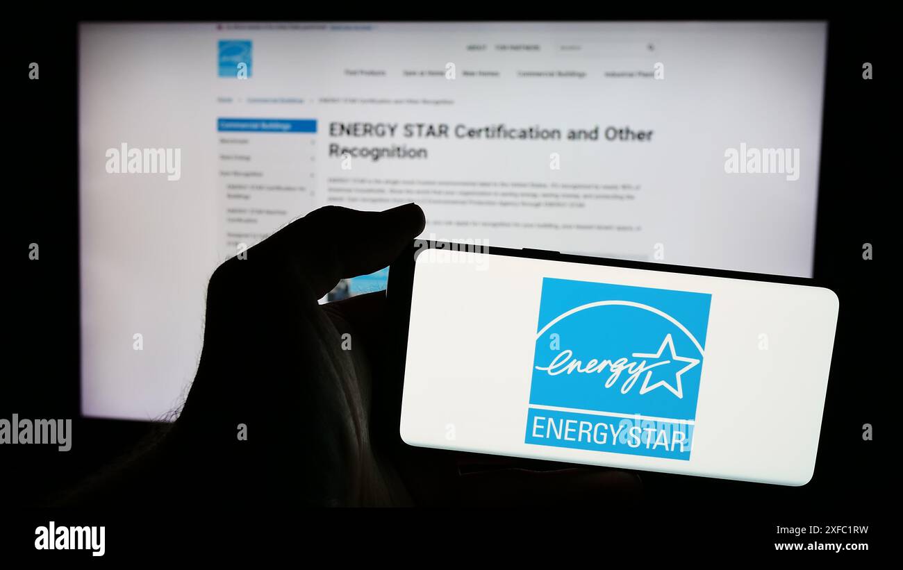Persona che possiede un telefono cellulare con il logo del programma di efficienza energetica statunitense Energy Star davanti alla pagina Web. Mettere a fuoco il display del telefono. Foto Stock