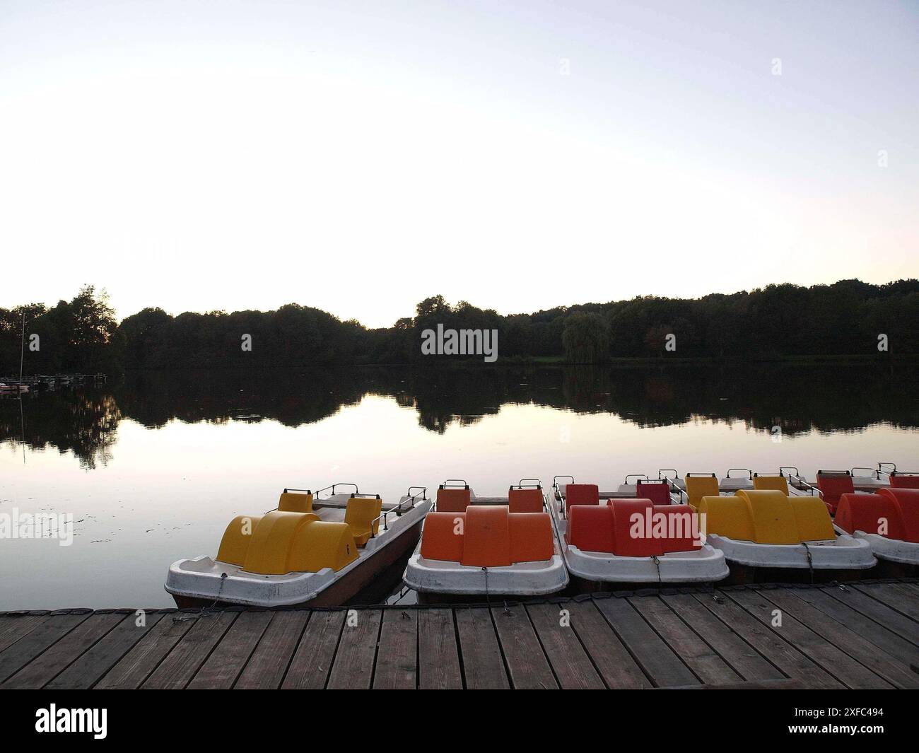 Diverse pedalò in giallo, arancione e rosso sulla riva del lago al tramonto, borken, germania Foto Stock