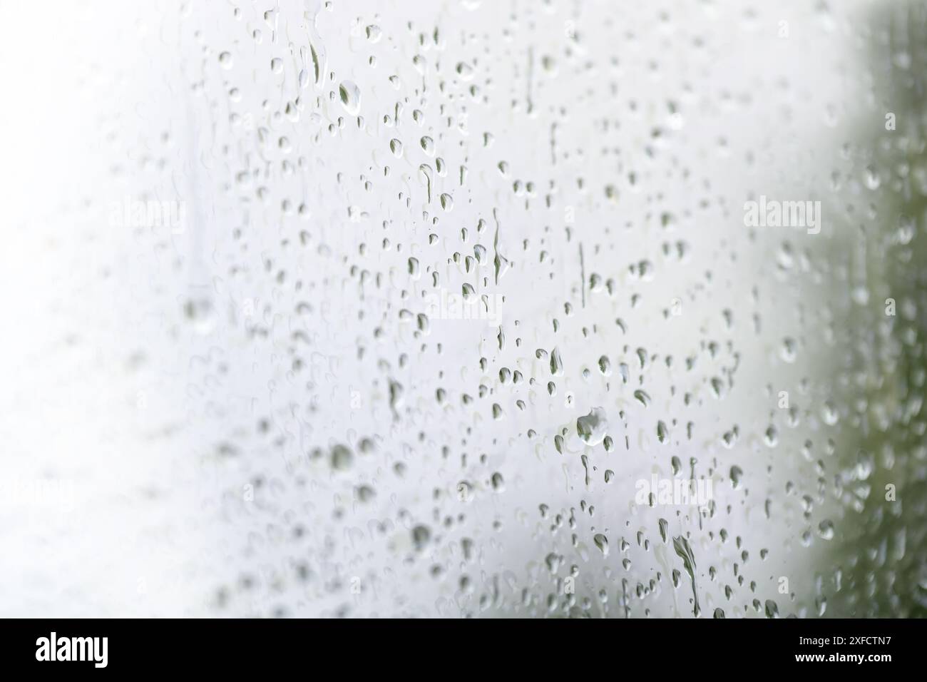 Gocce di pioggia su una finestra luminosa in un giorno di pioggia, condizioni meteorologiche e meteorologiche, spazio di copia, messa a fuoco selezionata con profondità di campo molto ridotta Foto Stock