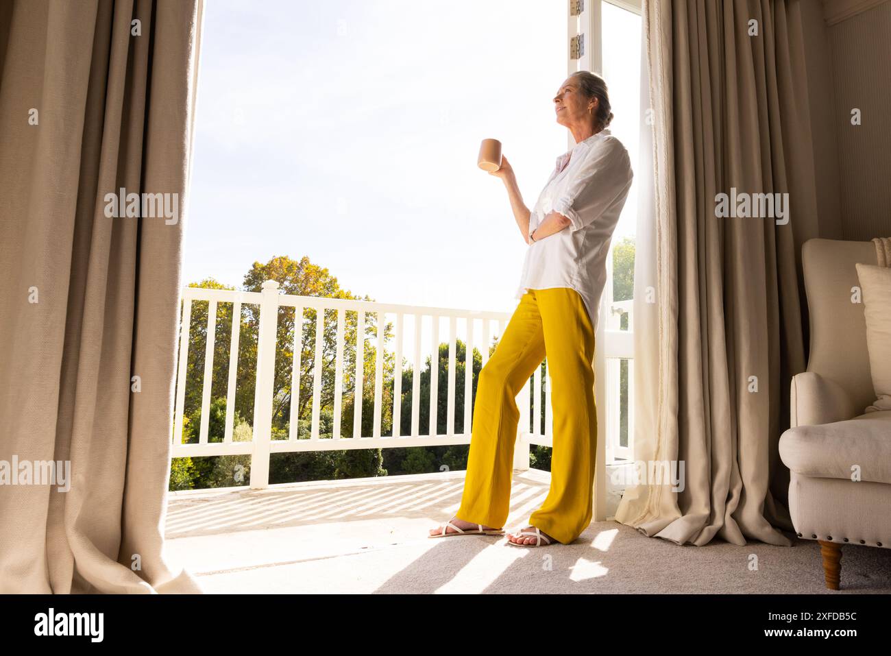 In piedi davanti a porte aperte, una donna anziana che si gusta il caffè mattutino a casa, spazio fotocopie Foto Stock