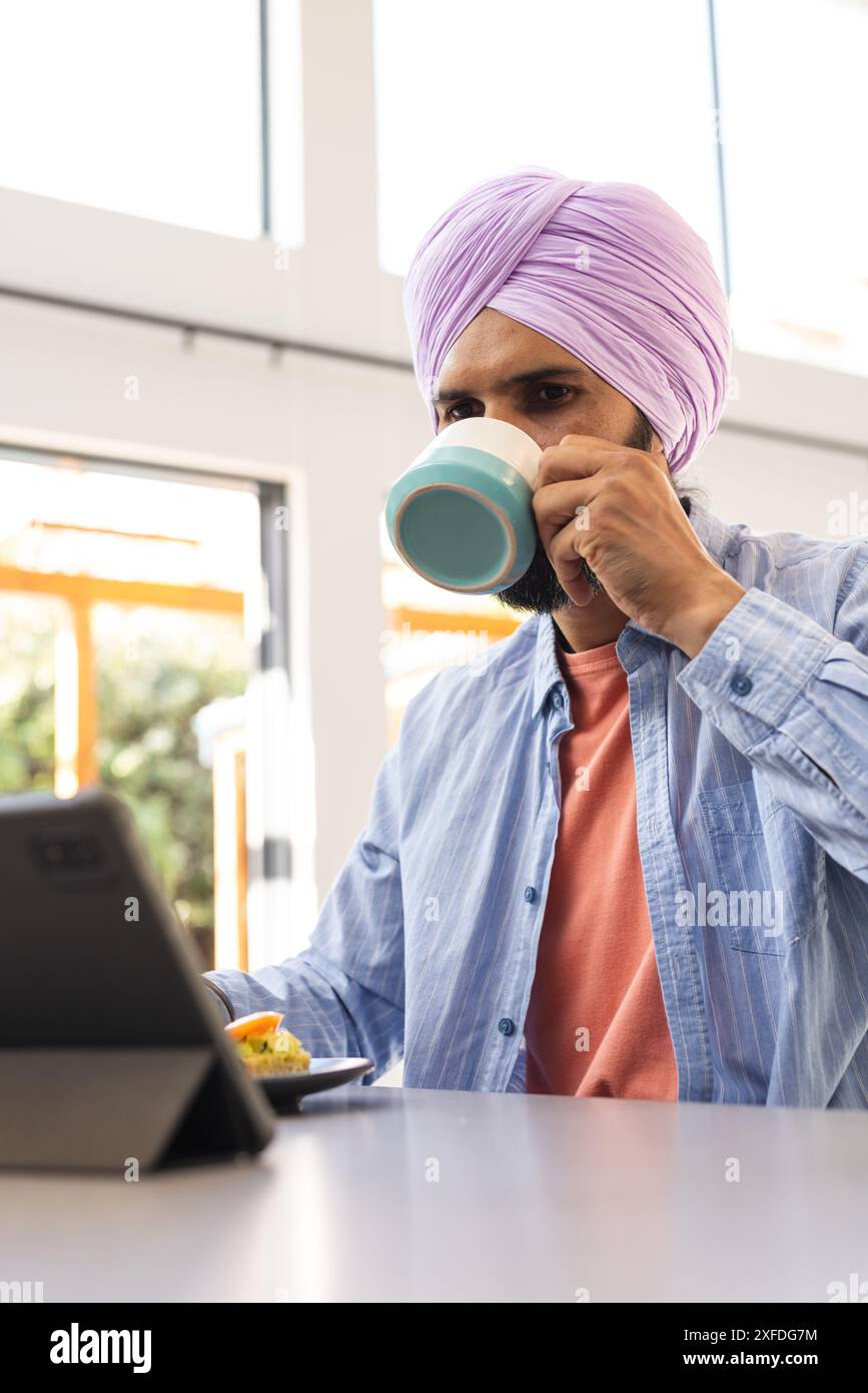 Bevendo caffè, uomo che usa un tablet mentre fa colazione a casa Foto Stock