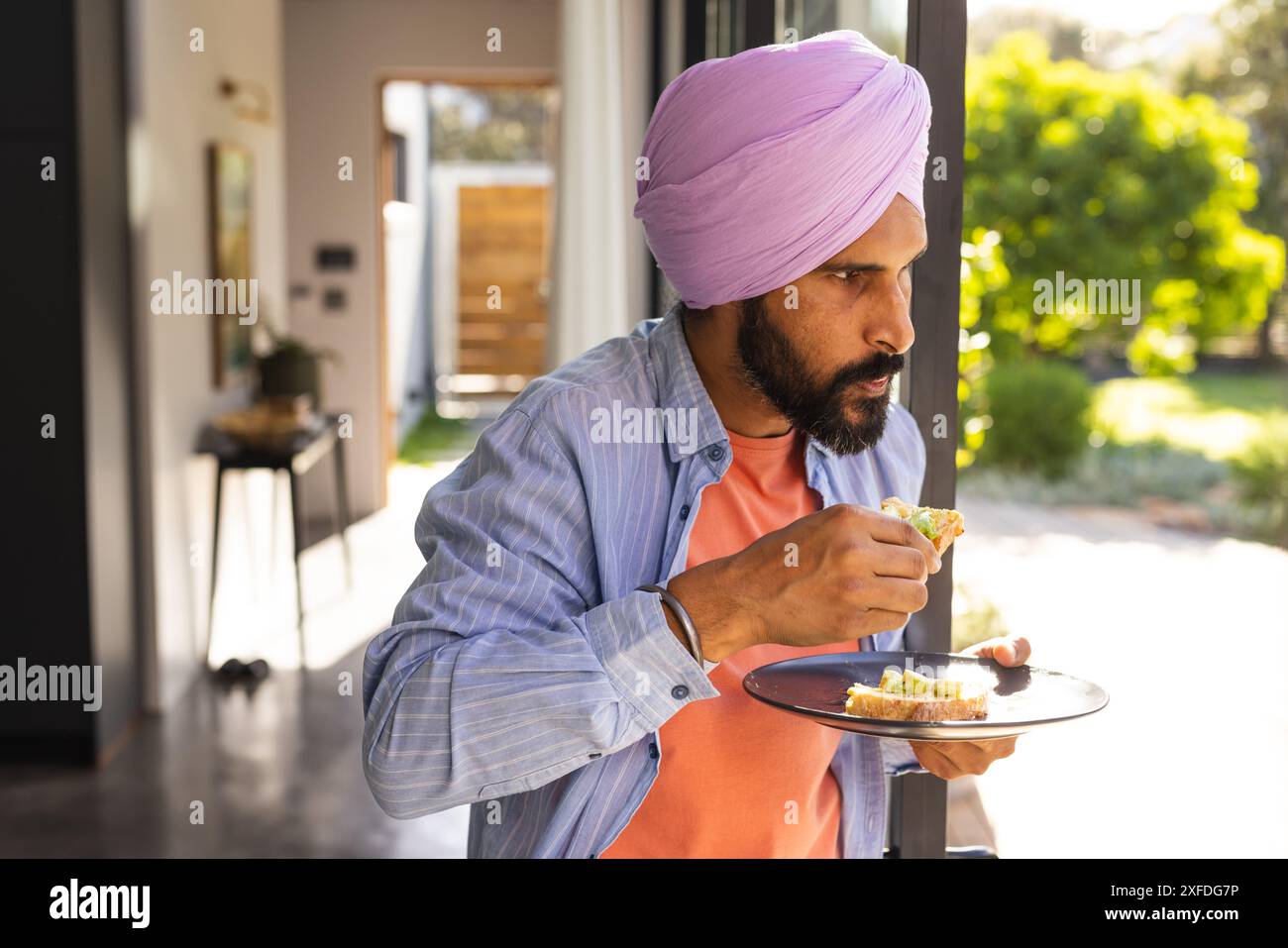 A fare colazione, uomo in turbante che tiene il piatto e sta vicino alla finestra Foto Stock