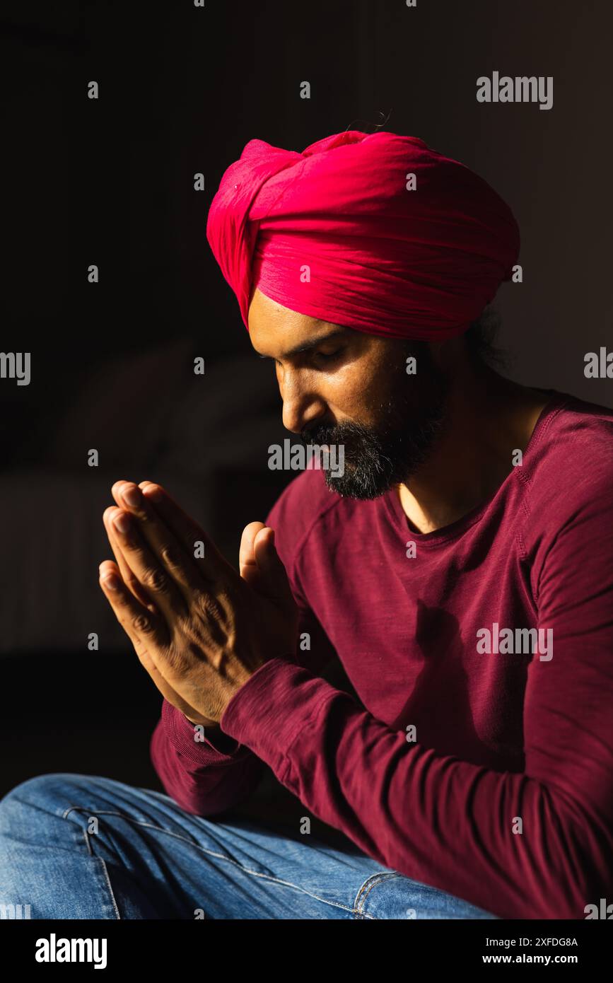 Pregando, uomo con turbante rosso e camicia marrone seduto con le mani insieme Foto Stock