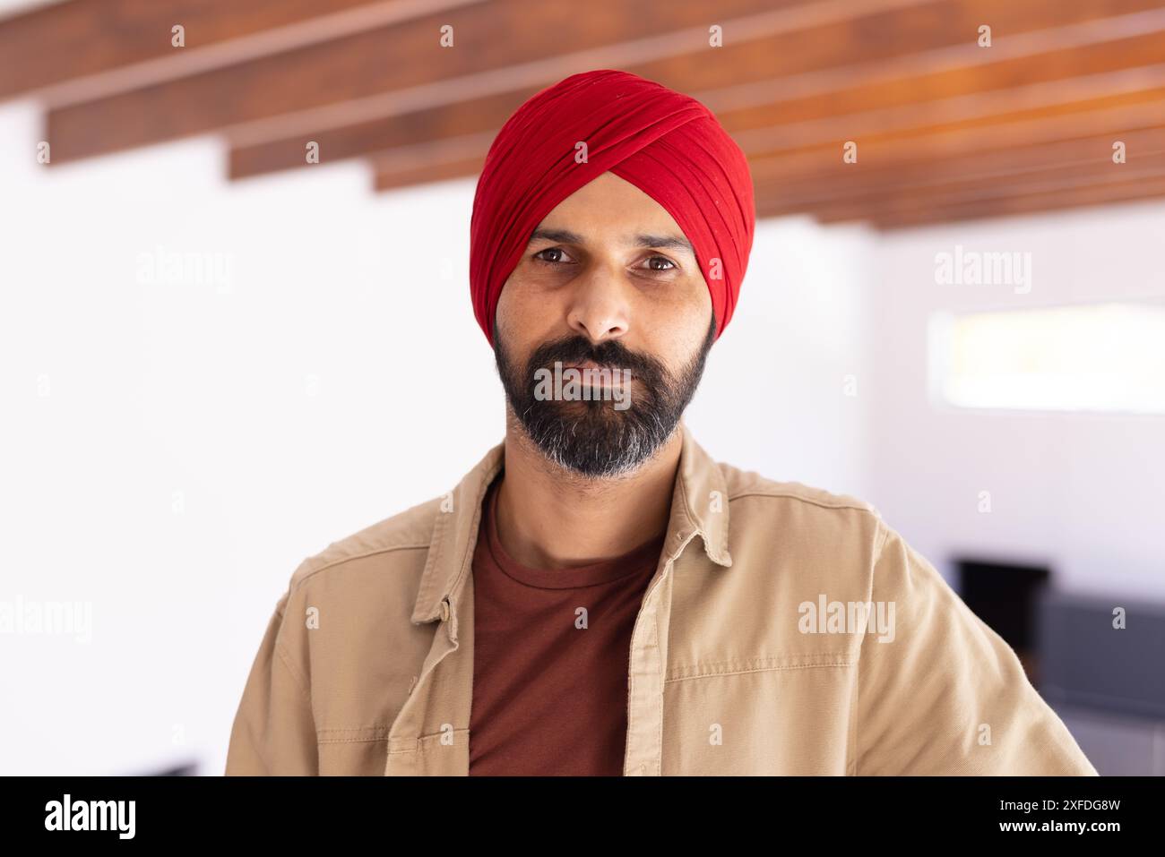Ritratto di un uomo indiano sicuro di sé che indossa un turbante rosso e abbigliamento casual al chiuso Foto Stock