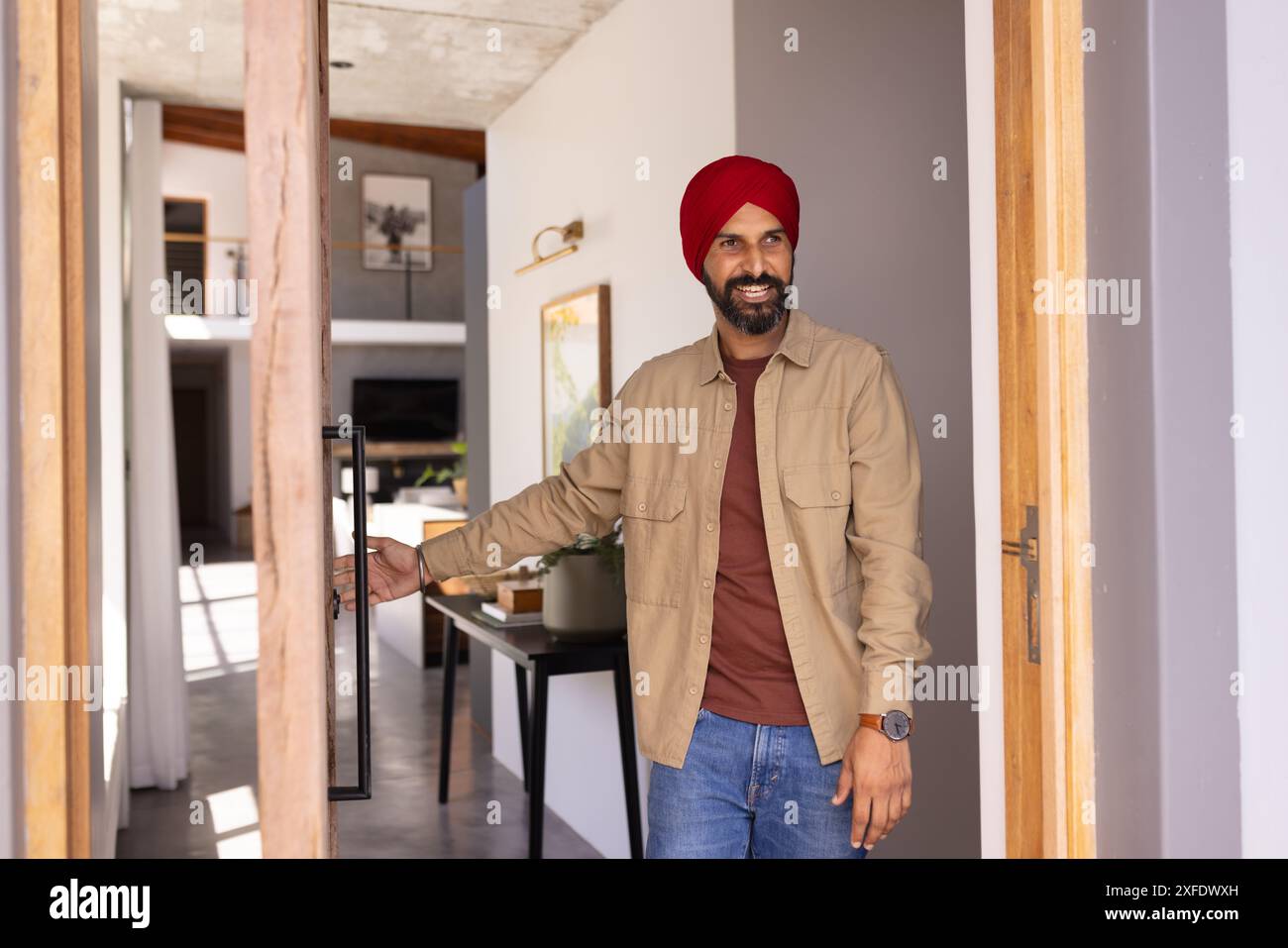 L'uomo che apre la porta e sorride accoglie gli ospiti in una casa moderna Foto Stock