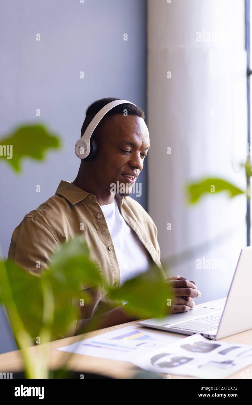 Utilizzando un computer portatile e indossando le cuffie, l'uomo partecipa a una riunione aziendale virtuale Foto Stock