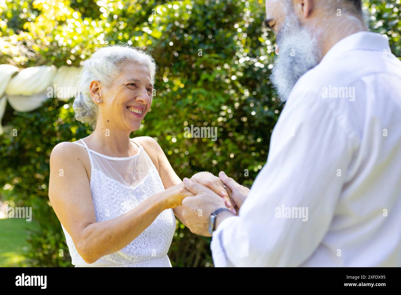 Sposa senior sorridente che si tiene per mano con lo sposo al matrimonio all'aperto Foto Stock