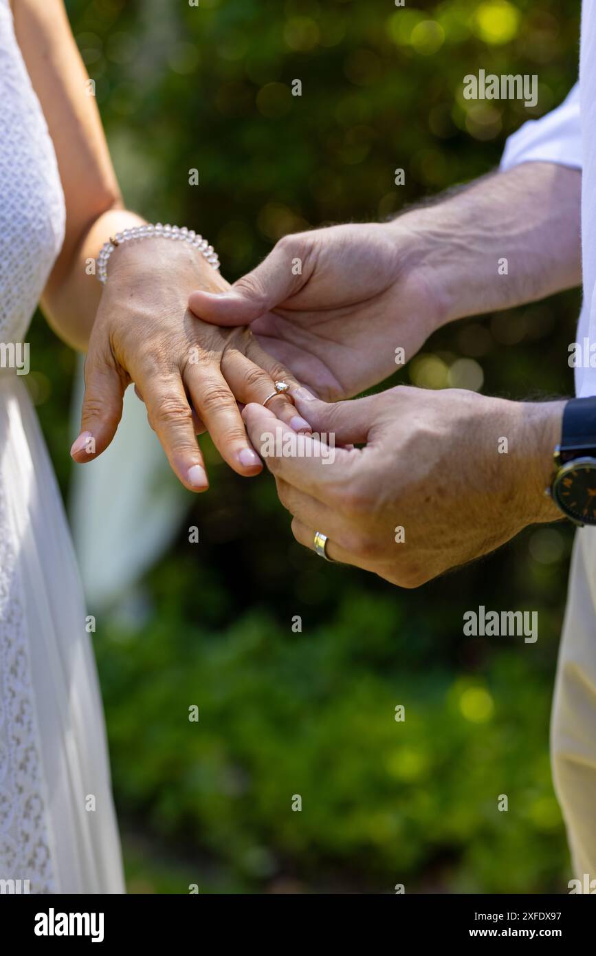 Scambiarsi le fedi nuziali, la sposa senior e lo sposo celebrano la cerimonia di matrimonio all'aperto con gioia Foto Stock