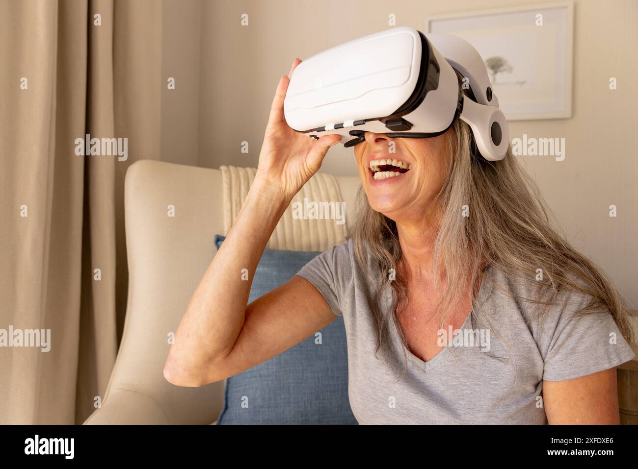 Utilizzando il visore VR, una donna matura si gode un'esperienza di realtà virtuale a casa Foto Stock