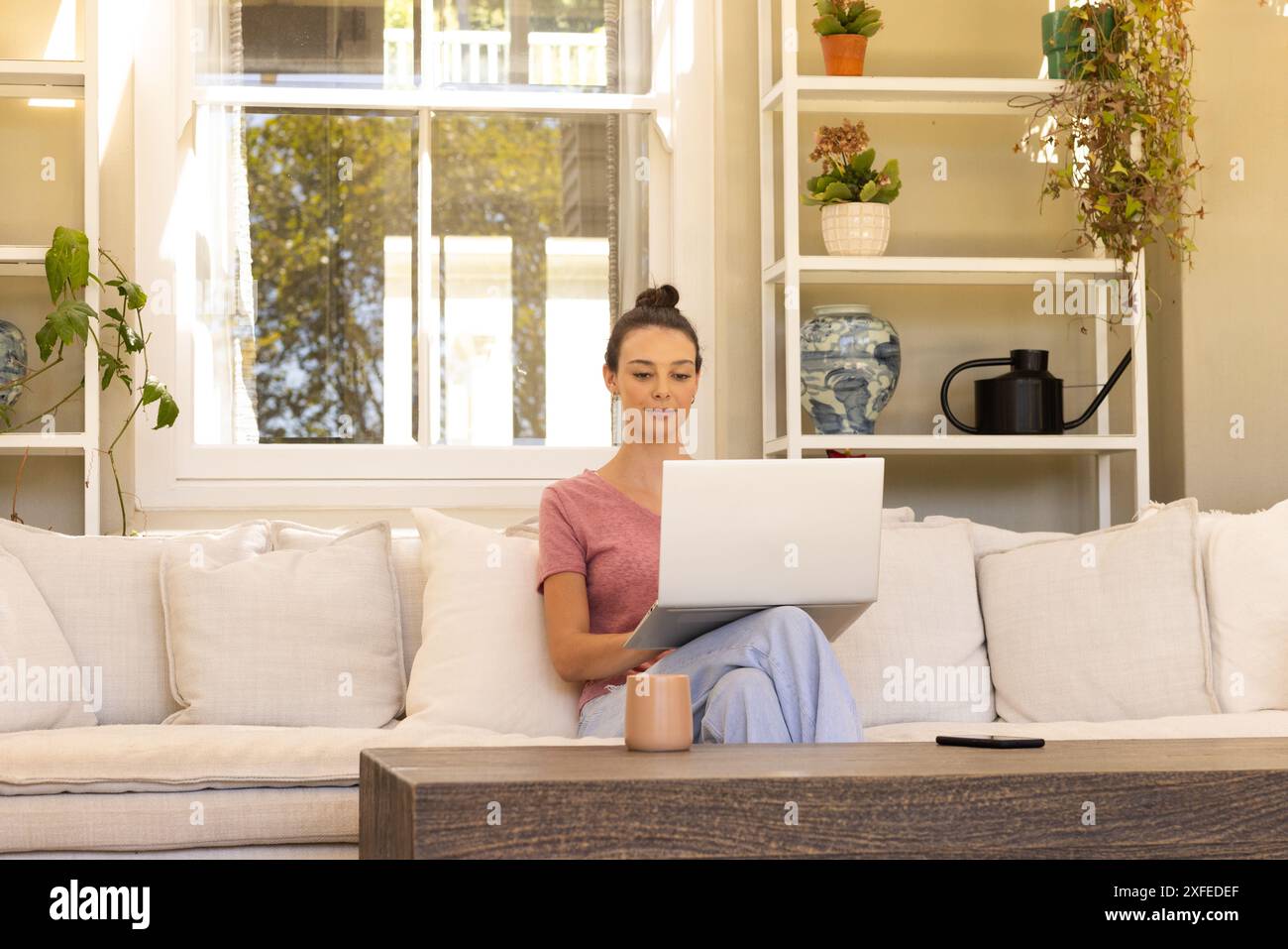 Lavora da casa, una giovane donna che usa il laptop sul divano con una tazza da caffè Foto Stock