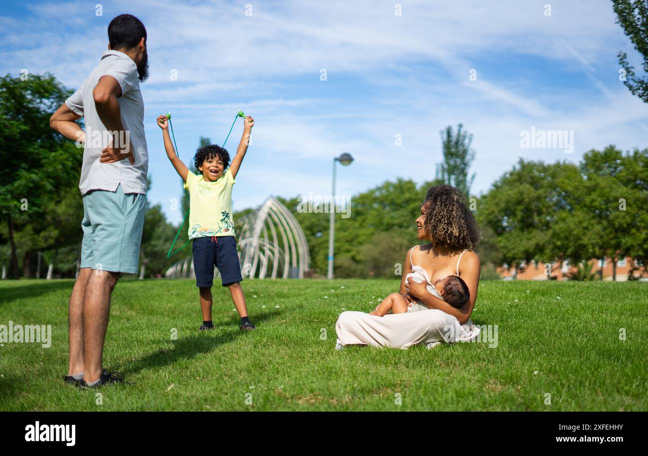Famiglia latina con due bambini che trascorrono la giornata in un parco all'aperto. Madre che allatta il suo bambino Foto Stock