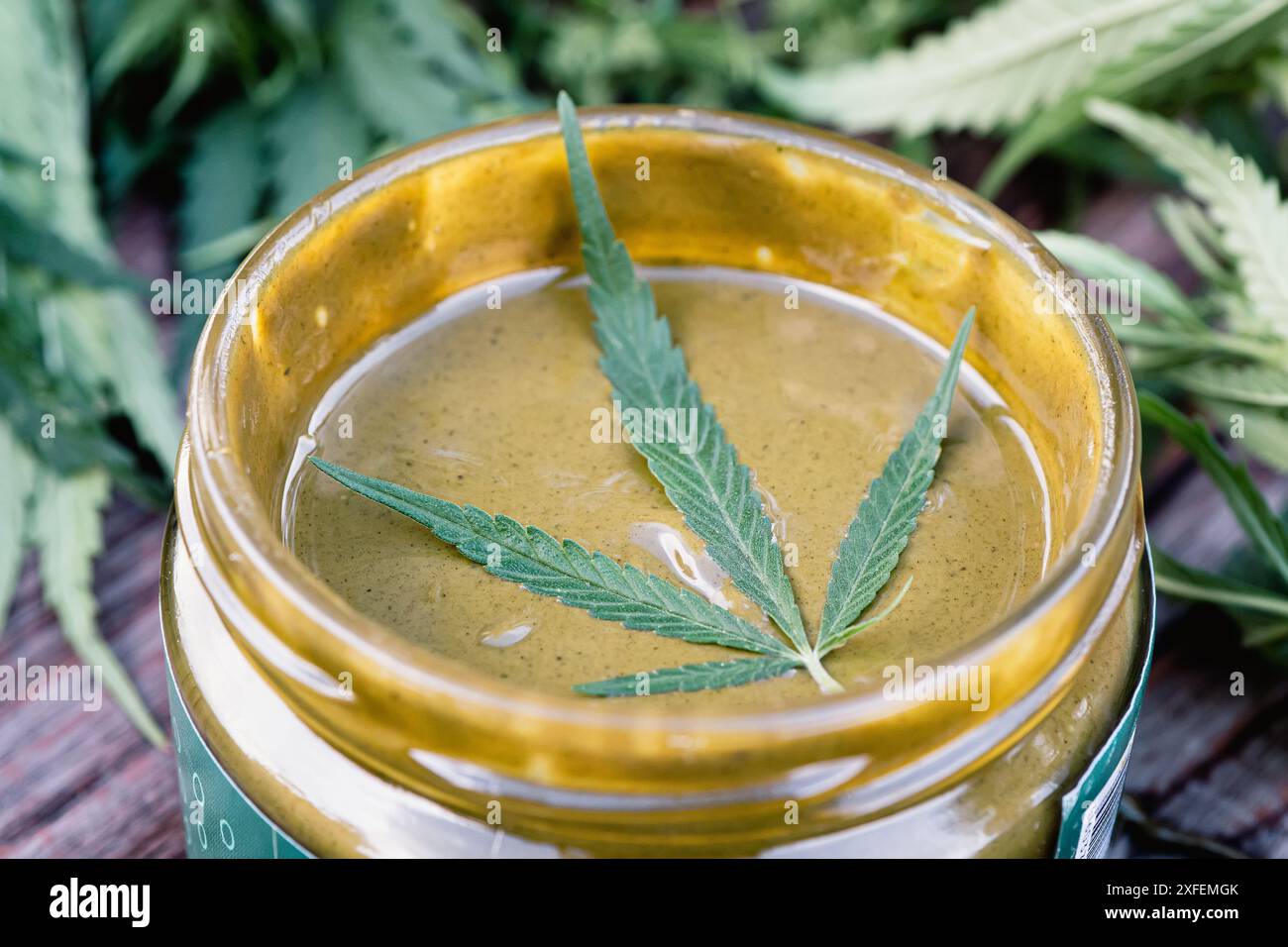 l'urbech preparata dai semi è stata scavata in un vaso di vetro su uno strato con foglie di marijuana. Deliziosa pasta verde dolce a base di canapa. Foto Stock