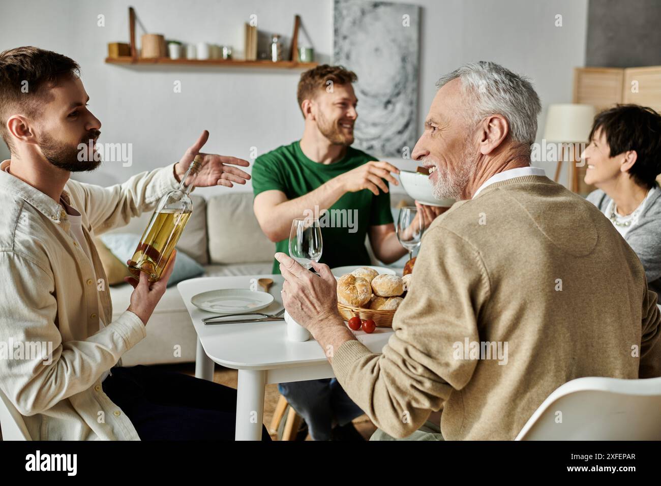 Una coppia gay condivide un pasto con i genitori a casa, godendosi un momento di amicizia e amore. Foto Stock