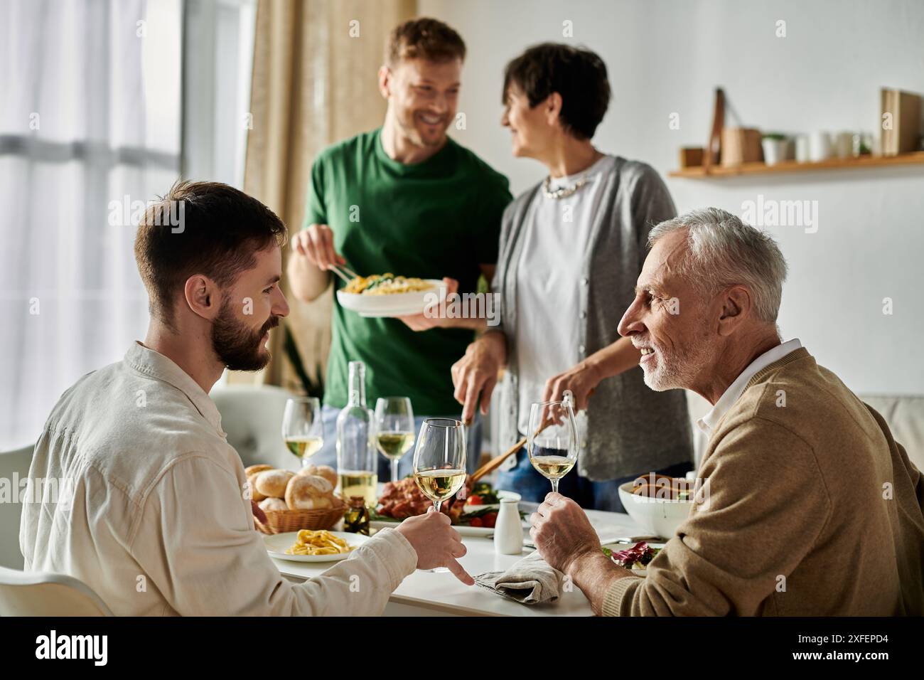 Una coppia gay condivide un pasto con i genitori, godendosi un momento di connessione e amore. Foto Stock