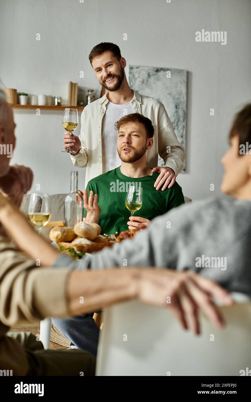 Una coppia gay si gode un pasto con i genitori a casa, alzando un bicchiere in un momento di commovente amicizia. Foto Stock