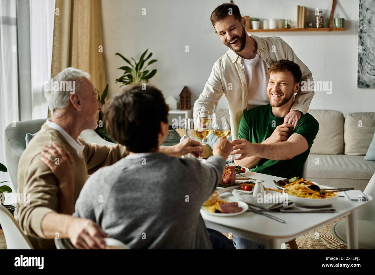 Una coppia gay si gode un pasto con i genitori a casa, alzando i bicchieri in un brindisi. Foto Stock